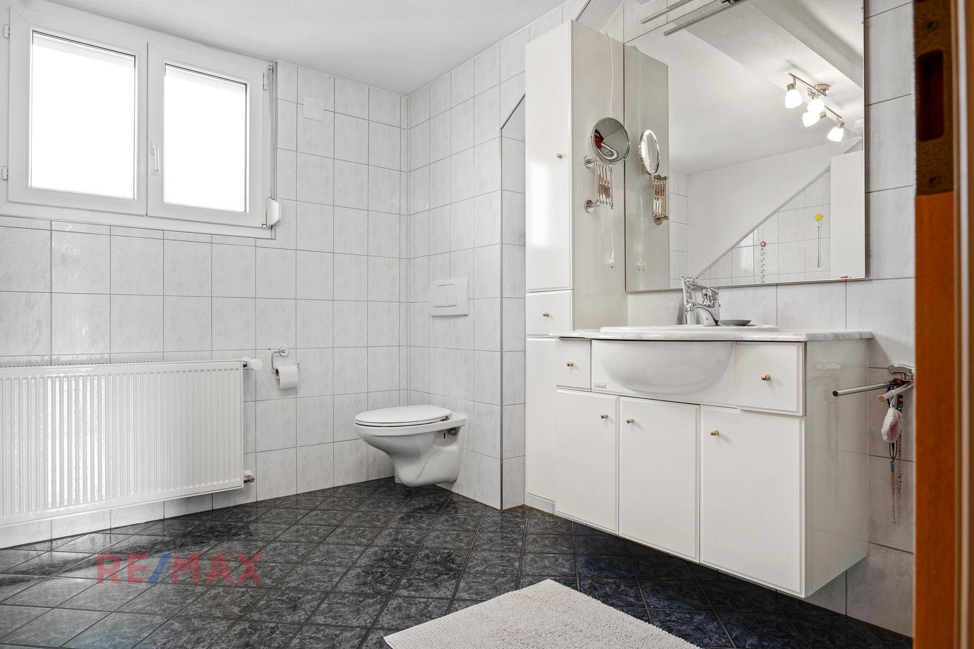 Modernes Badezimmer mit weißen Wandfliesen, dunklem Boden und Fenster.