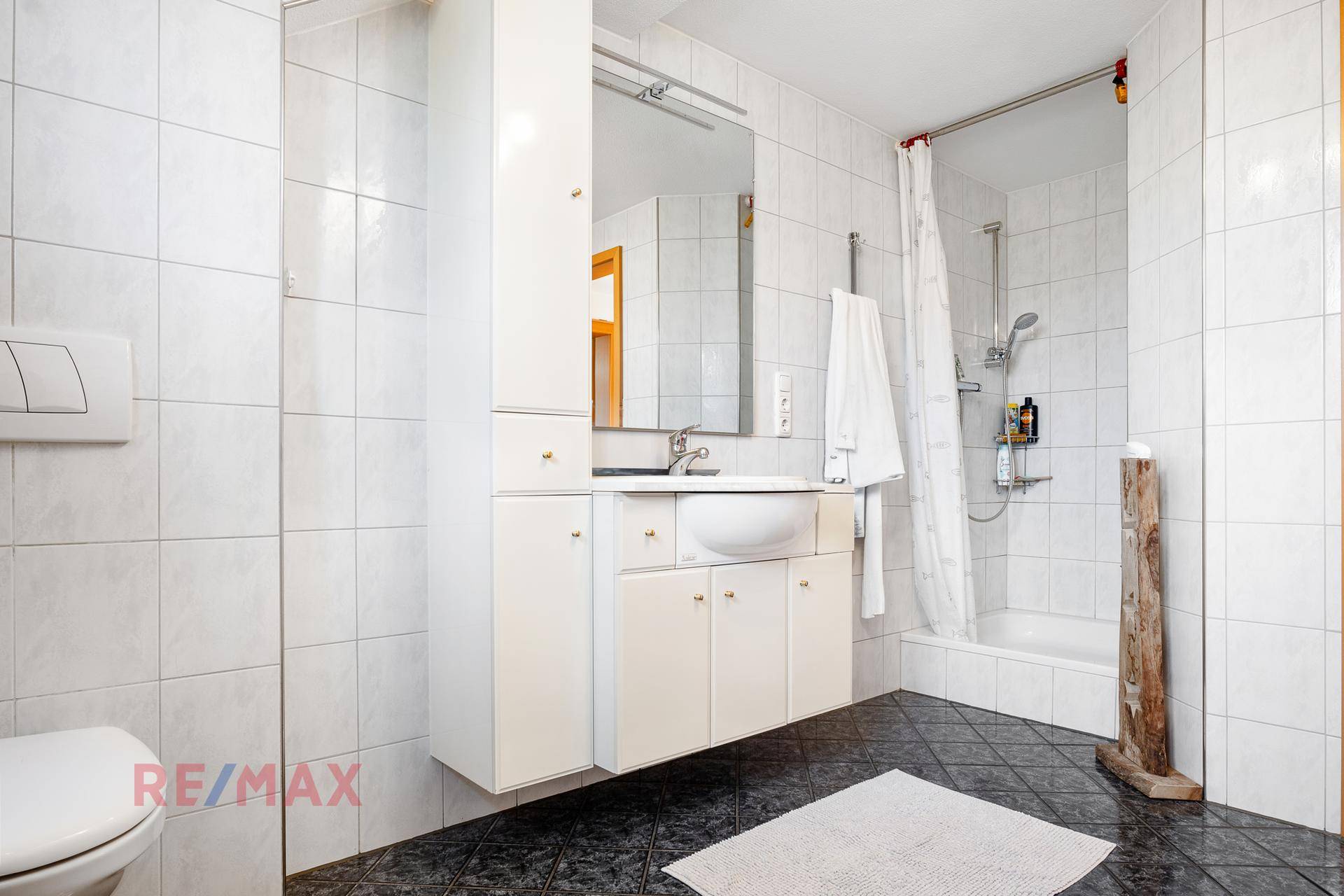Badezimmer mit weißer Duschwanne, weißen Wandfliesen und dunklem Boden.
