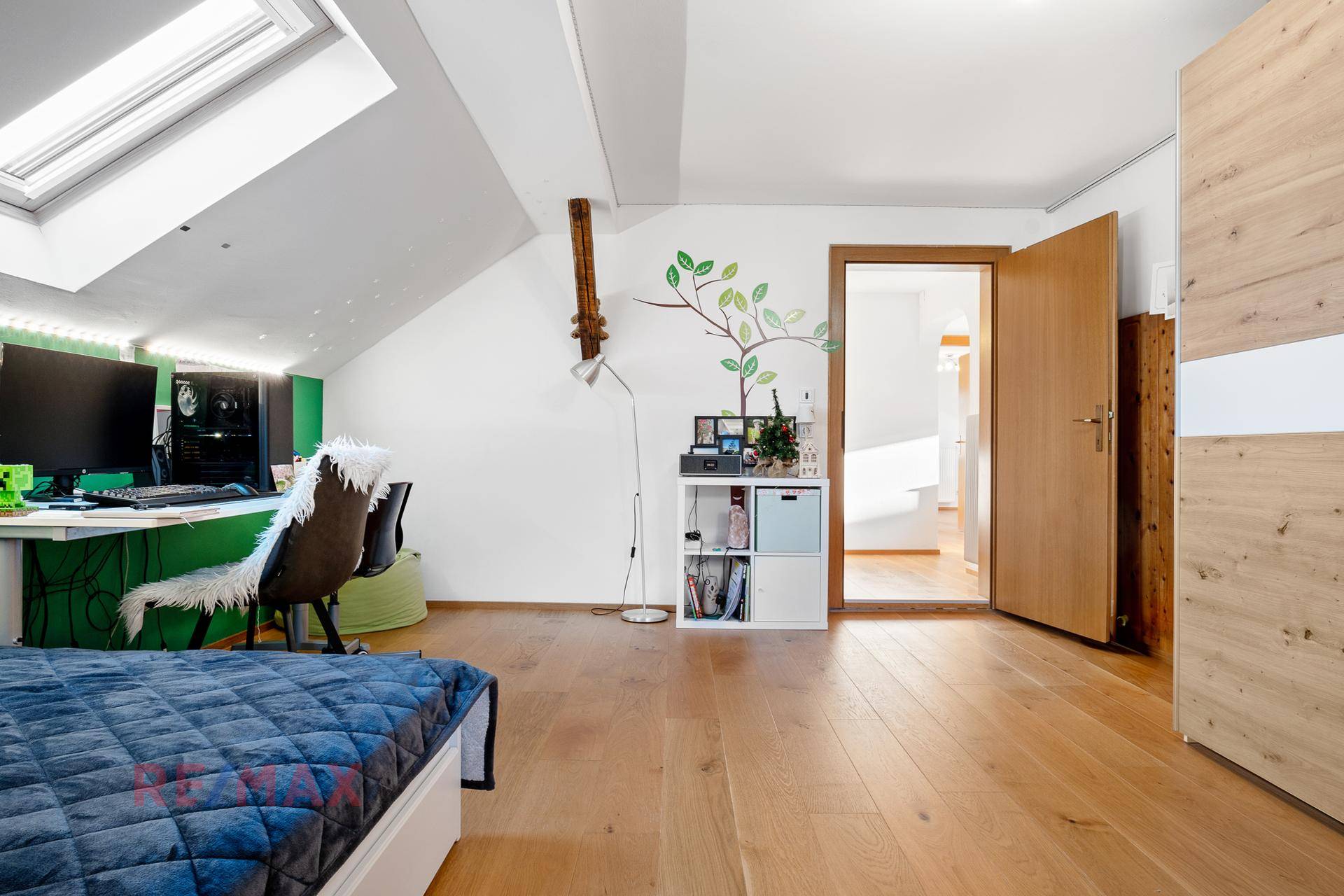 Kinderzimmer mit Holzboden, grüner Akzentwand, Dachfenster und Zugang zum Flur.