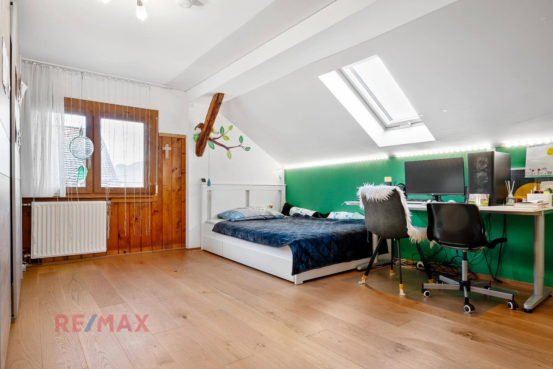 Helles Kinderzimmer mit Holzboden, grüner Akzentwand, Dachfenster und Schreibtisch.