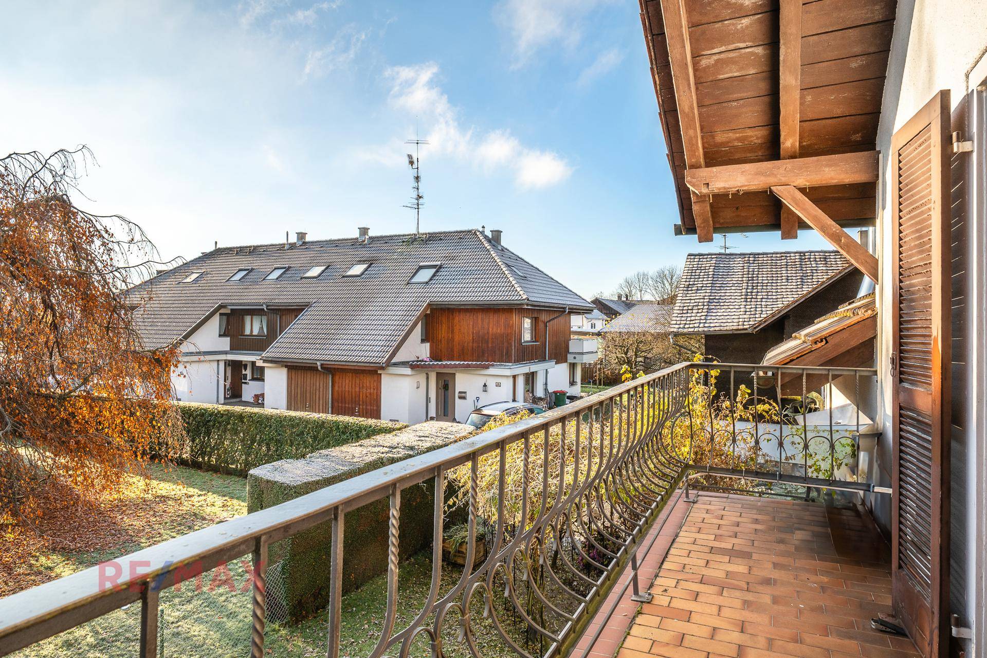 Balkon mit schmiedeeisernem Geländer, Ziegelboden und Blick auf die Nachbarschaft.