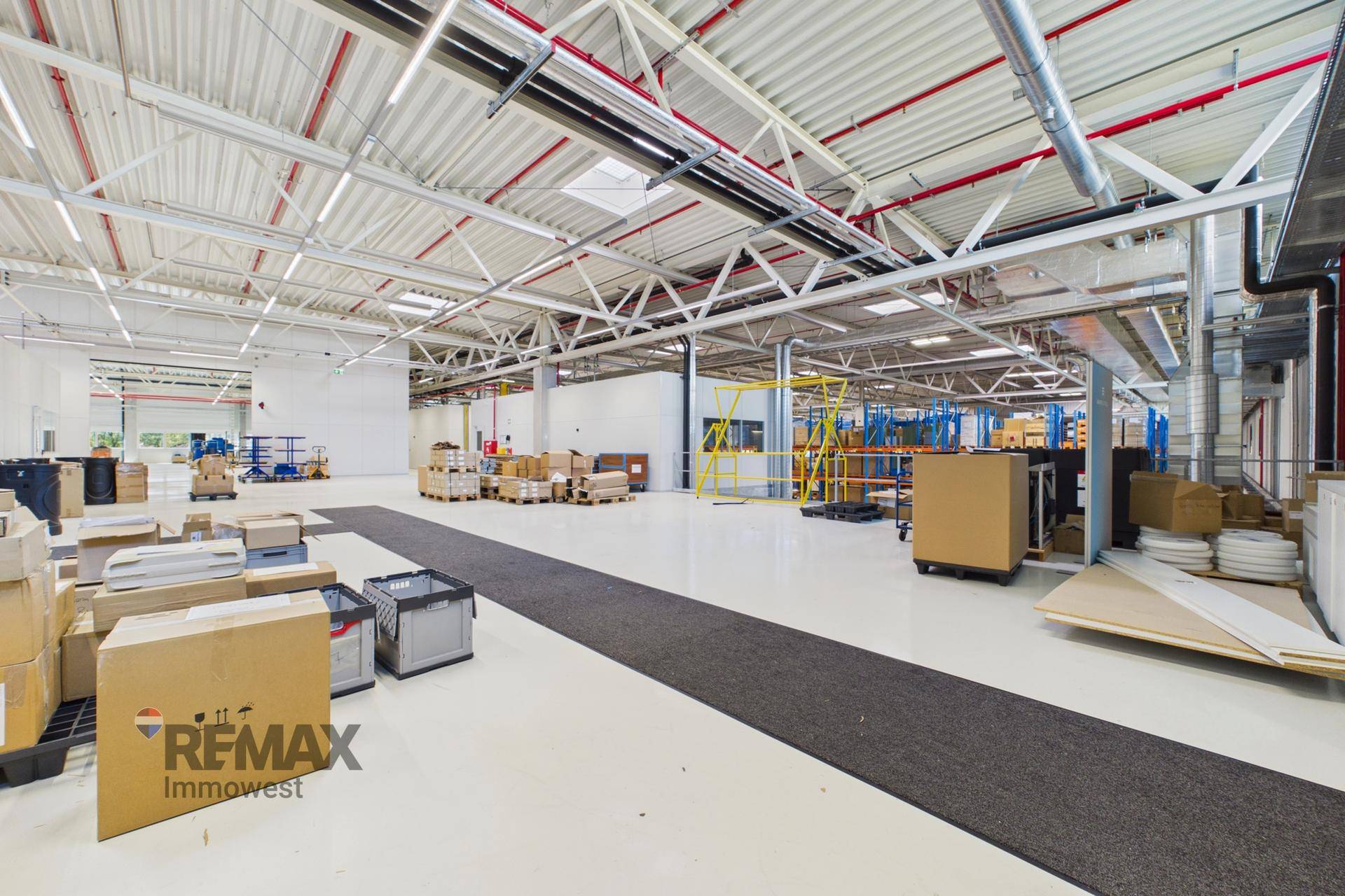 Weitläufige Lagerhalle mit hohem Deckenbereich, weißem Boden, dunklem Teppichpfad und industrieller Ausstattung.