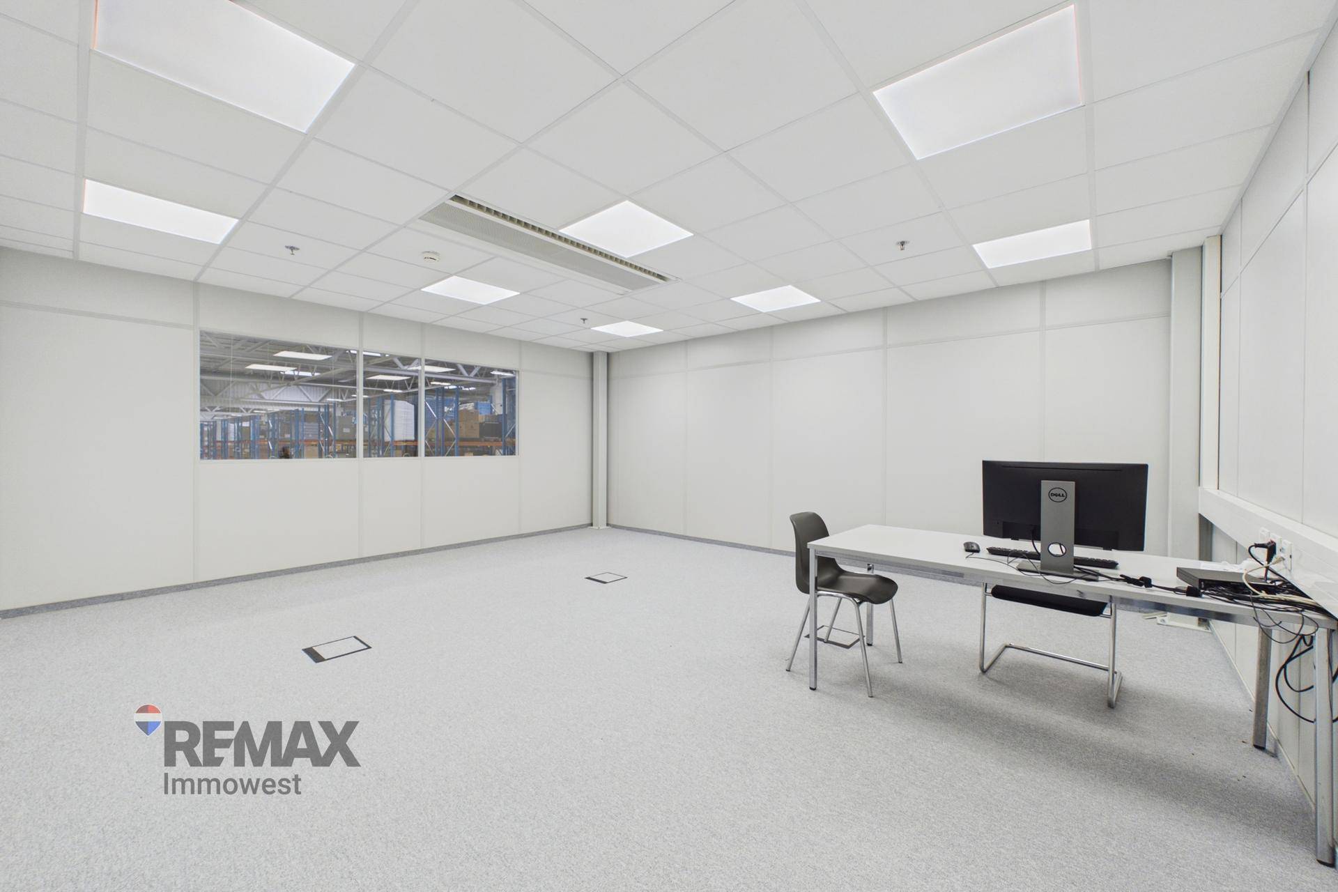 Modernes, helles Büro mit einem Schreibtisch, Computer und Blick in die Produktionshalle.