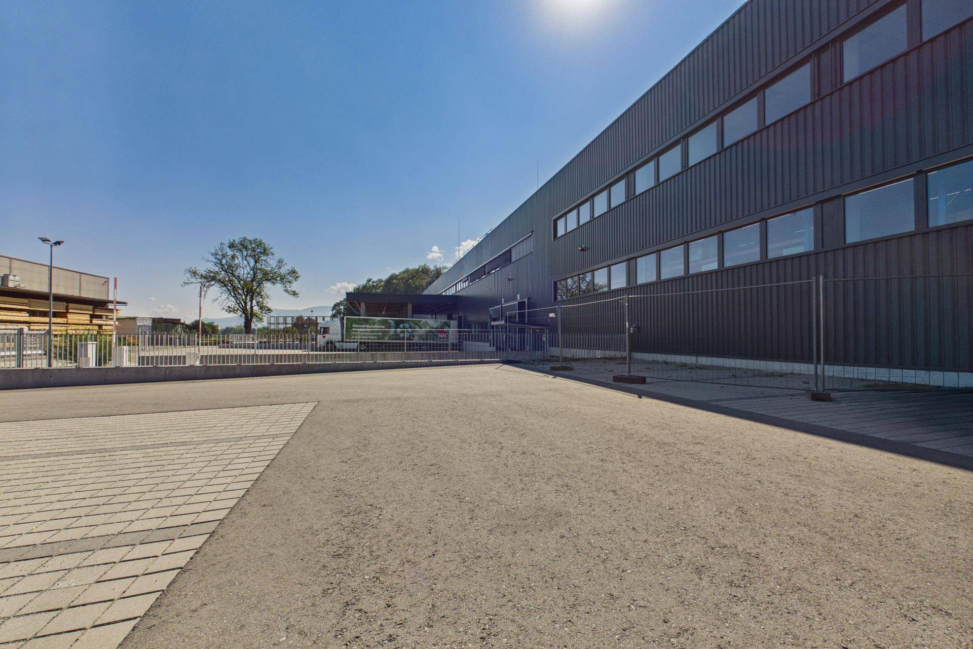 Außenansicht des modernen Gebäudes mit dunkler Fassade, großem Parkplatz und sonnigem Wetter.