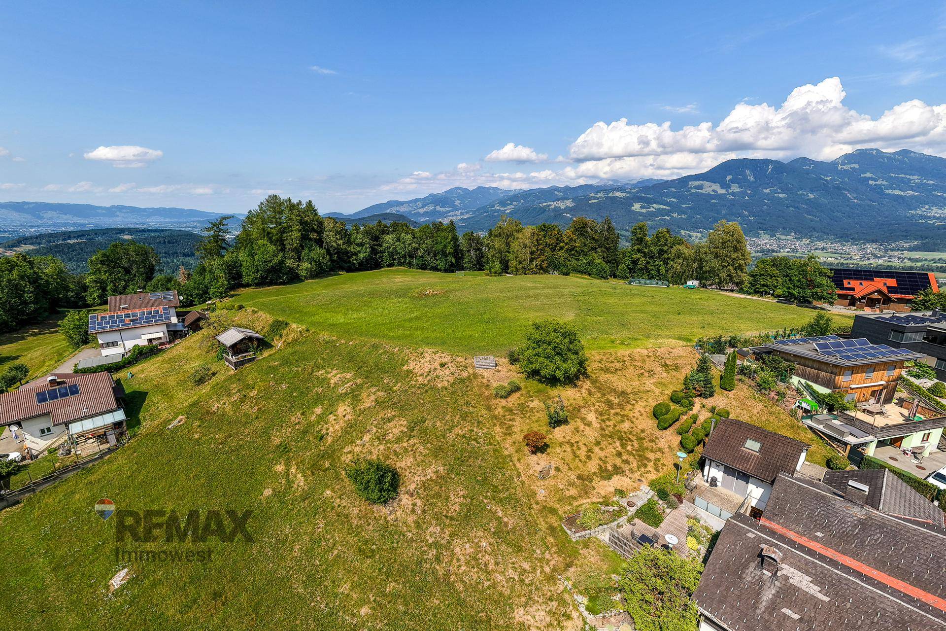 Idyllische Landschaft mit sanften Hügeln, vereinzelten Häusern und majestätischen Bergen am Horizont.