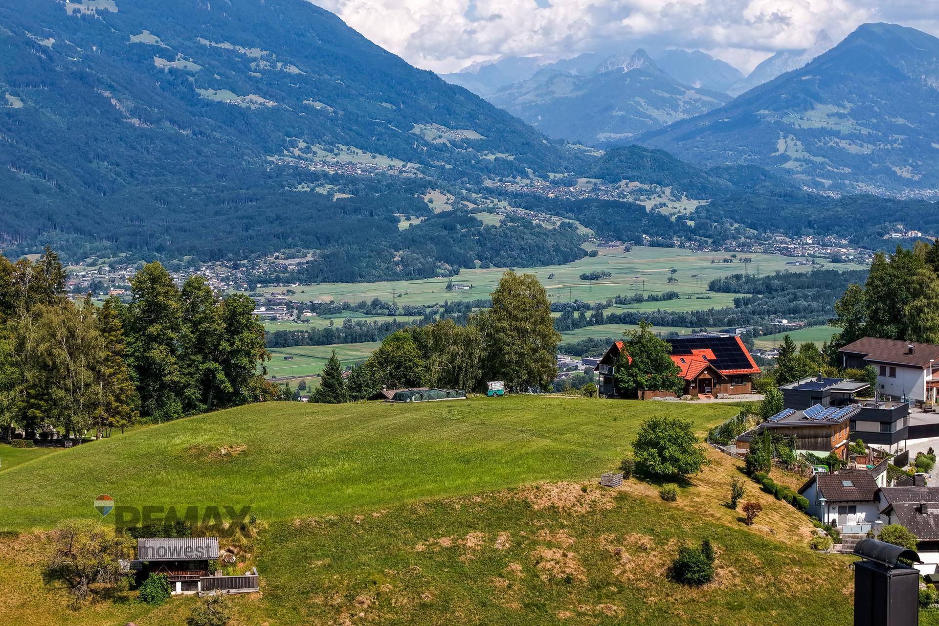 Sonnige Landschaft mit grünen Hügeln, verstreuten Häusern und einem weiten Blick ins Tal.