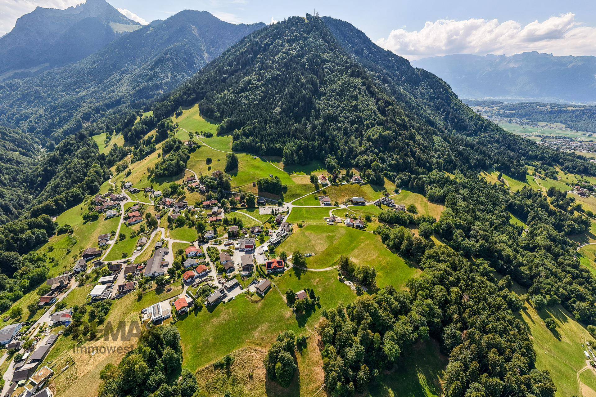 Majestätischer Berg mit bewaldeten Hängen und verstreuten Häusern, die sich in die Landschaft einfügen.