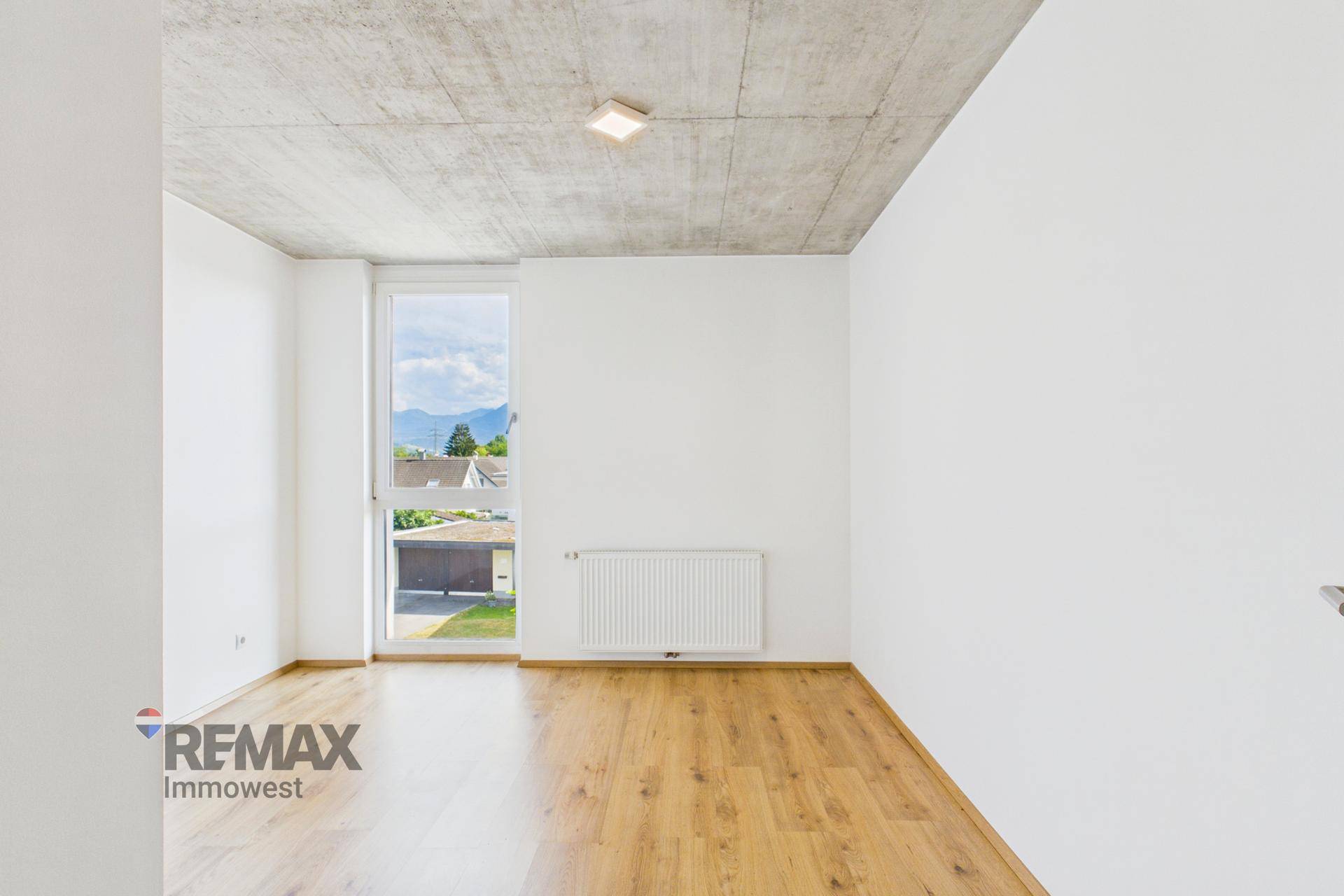 Helles Schlafzimmer mit Holzfußboden, großem Fenster und Heizkörper.