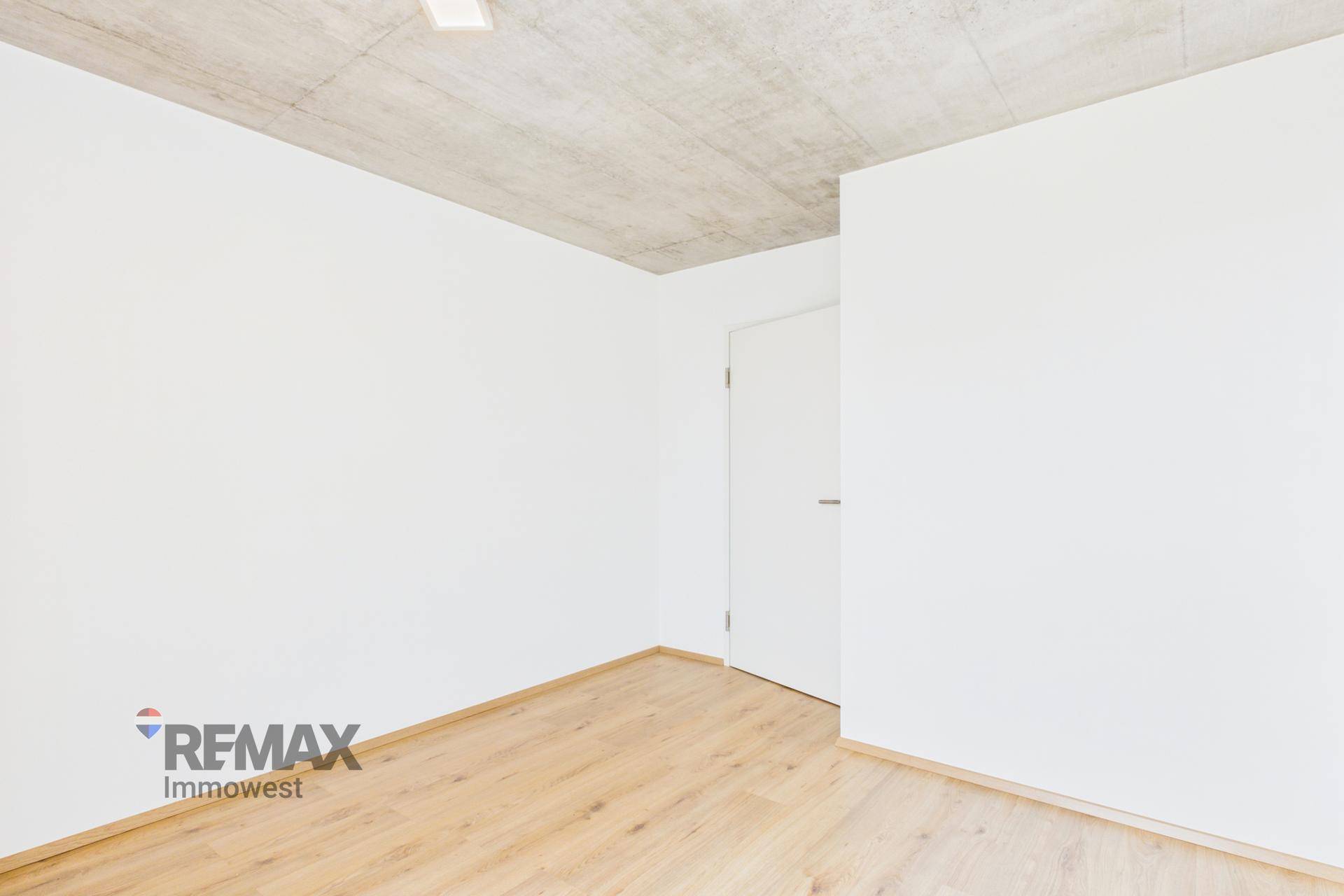 Leeres Zimmer mit hellem Holzfußboden und weiß gestrichenen Wänden.