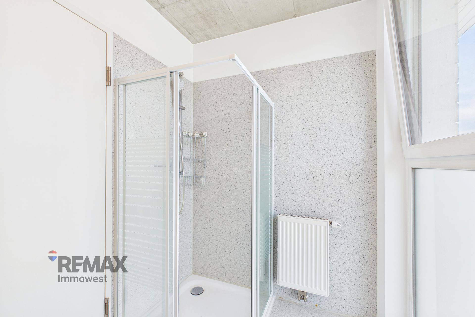 Badezimmer mit Duschkabine, hellen Fliesen und Heizkörper.