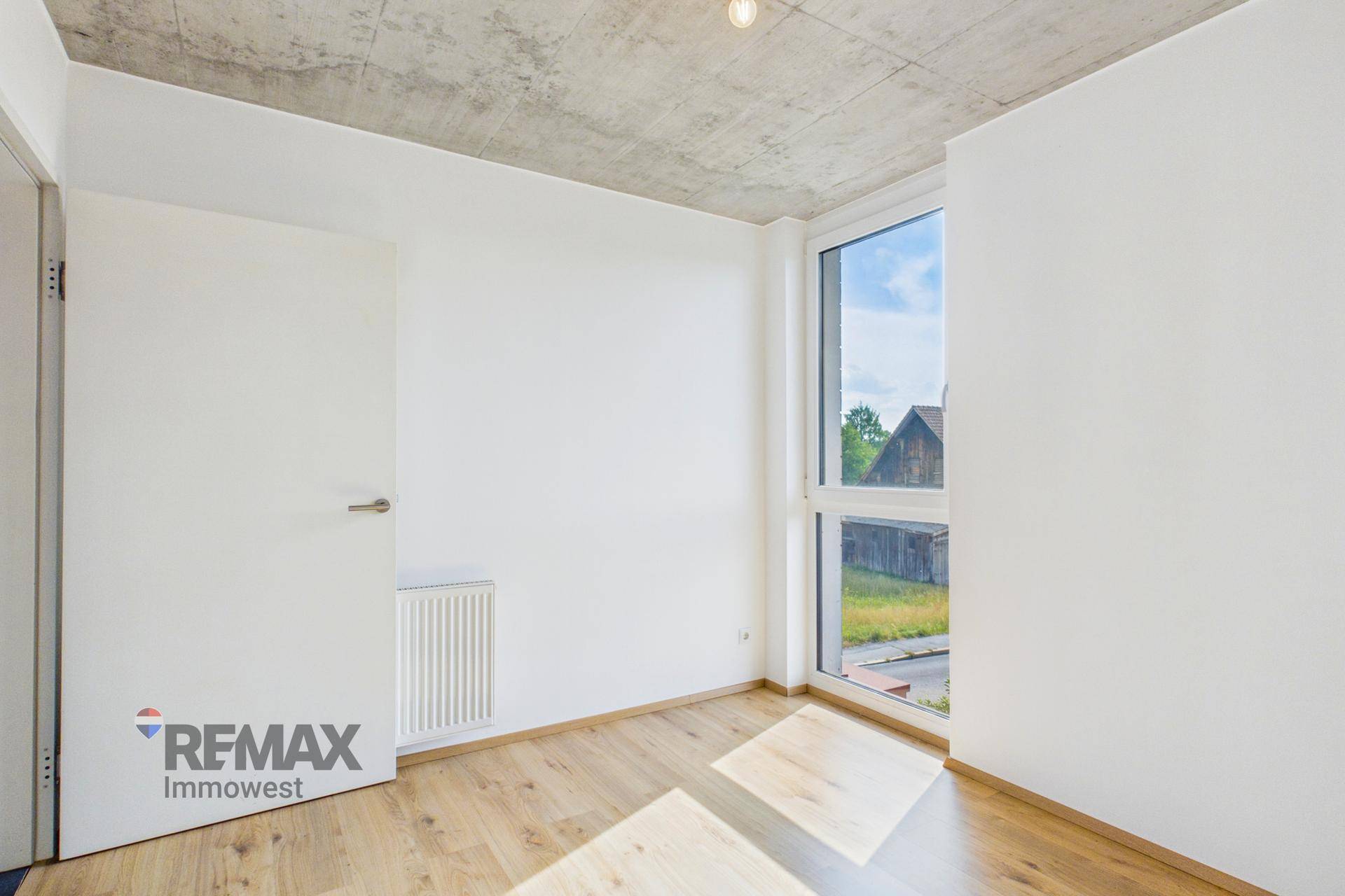 Helles Zimmer mit Holzboden, weißer Tür und Heizung unter dem Fenster.