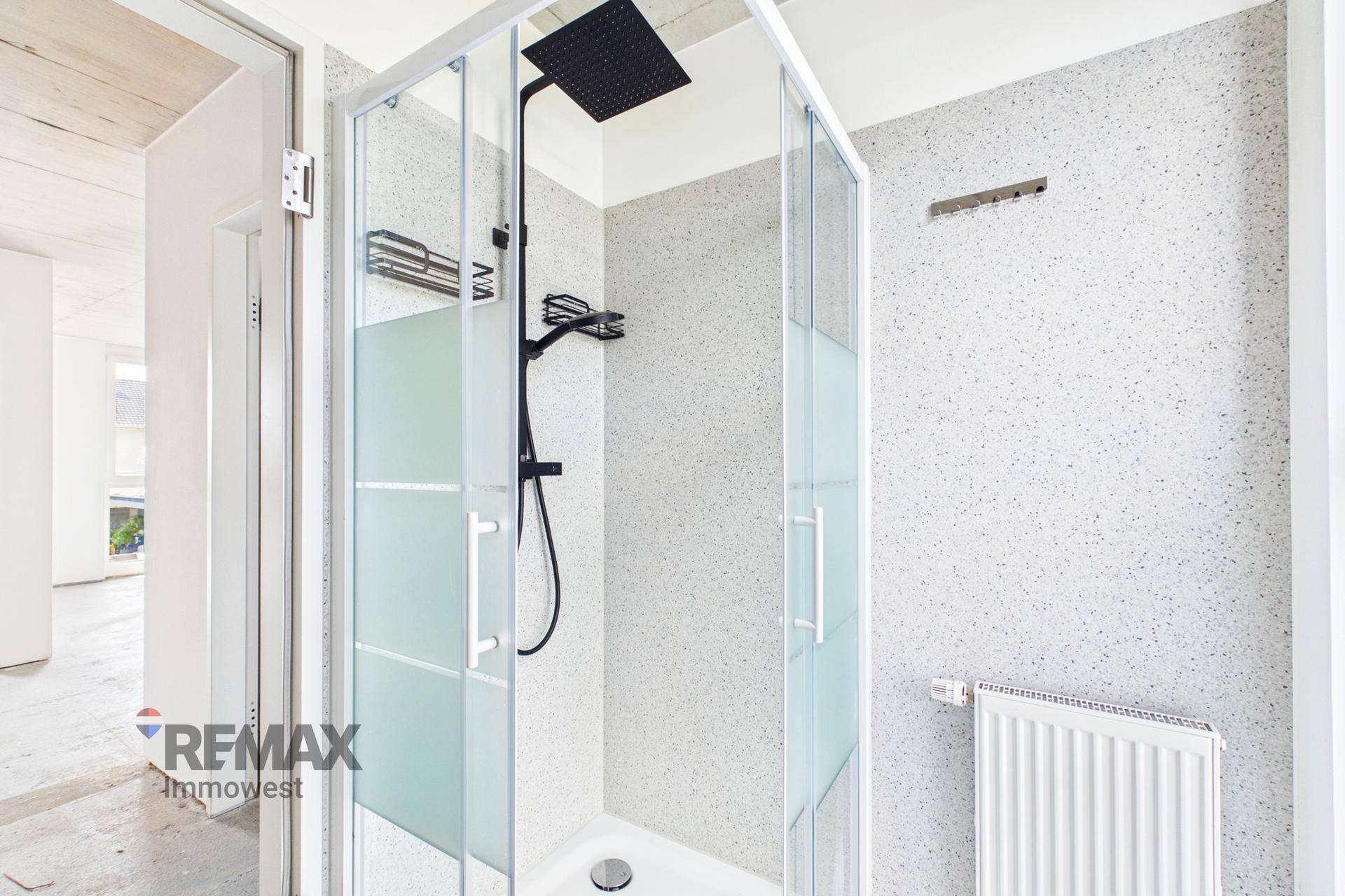 Modernes Badezimmer mit einer geräumigen Duschkabine und schwarzem Regenduschkopf.