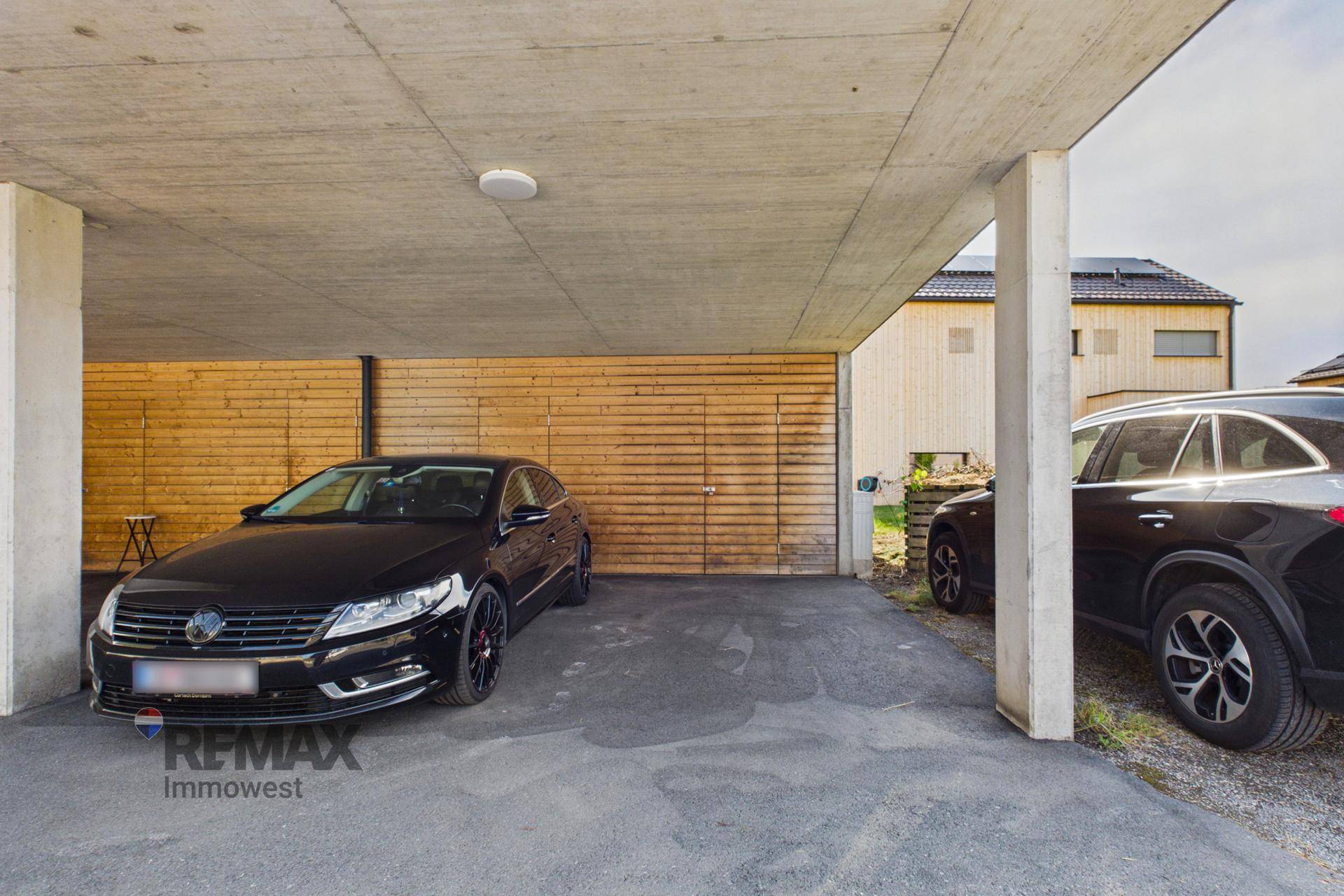 Überdachter Parkplatz mit zwei Fahrzeugen und Holzwand im Hintergrund, bietet Schutz vor Witterung.