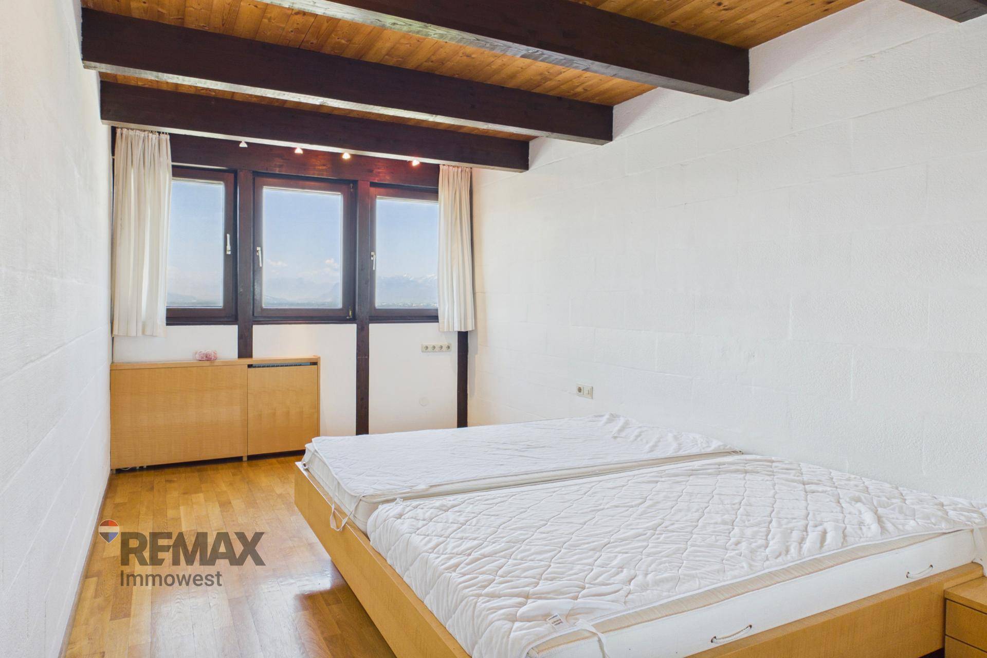 Schlafzimmer mit Doppelbett, Holzbalkendecke und Fenstern mit Blick ins Grüne.