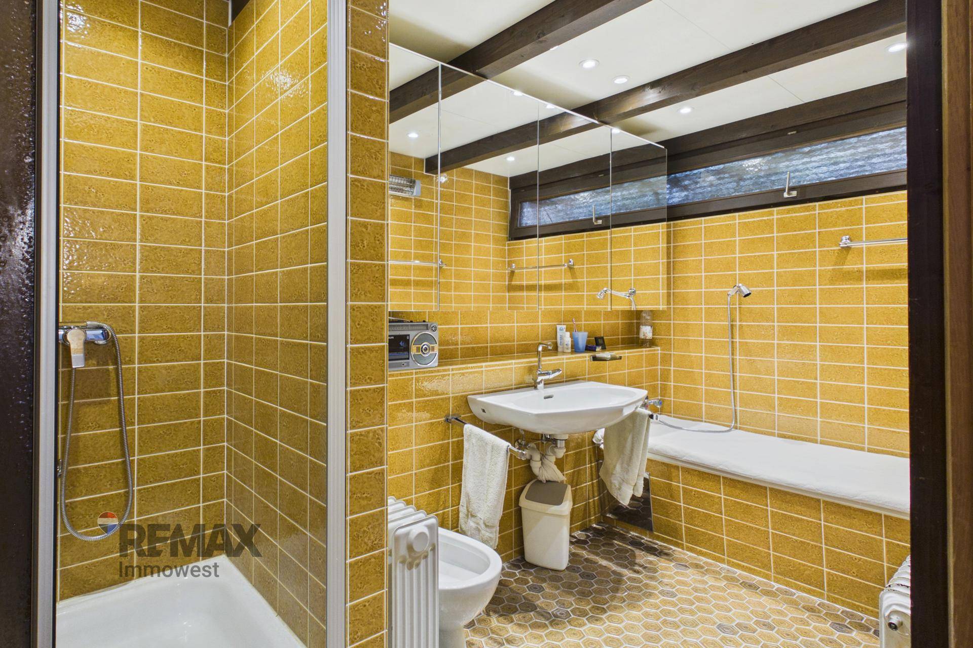 Badezimmer mit gelben Fliesen, Dusche, Waschbecken, WC und Bidet in funktionalem Design.