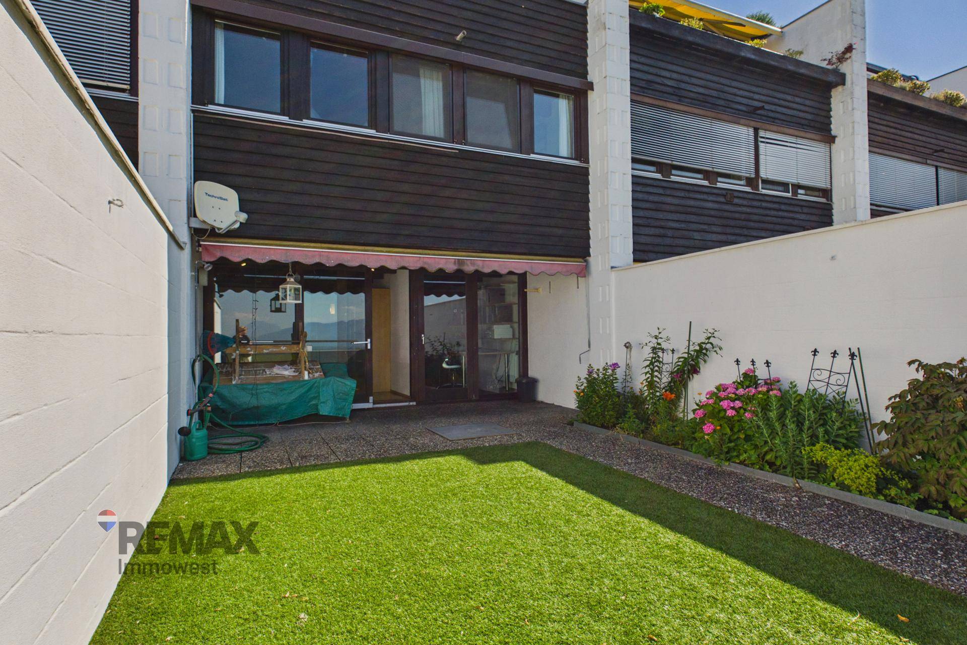 Rückseite des Hauses mit kleinem Garten, Terrasse und Markise.