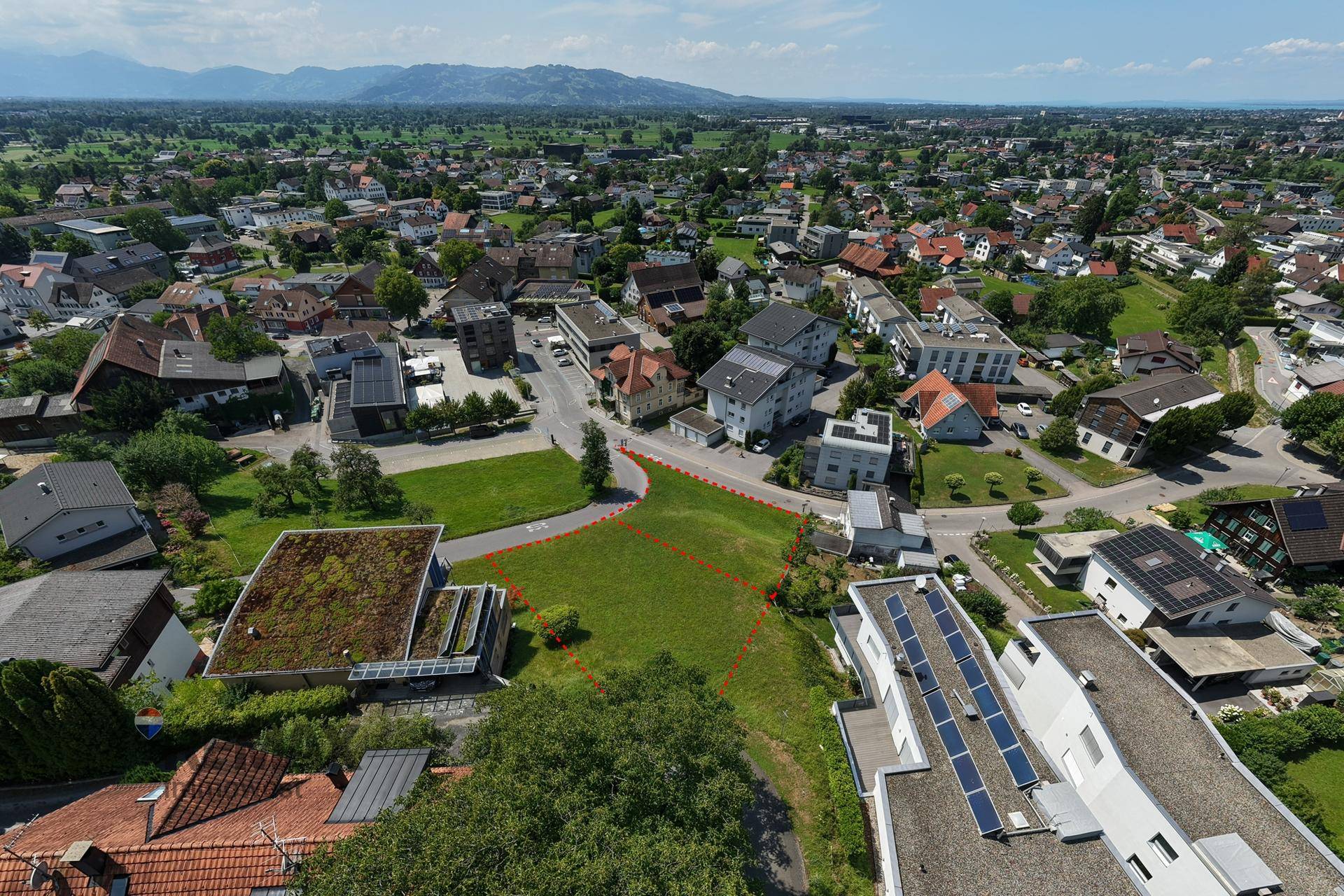 Luftaufnahme des Baugrundstücks mit Blick über die Stadt und die ferne Bergkette am Horizont.