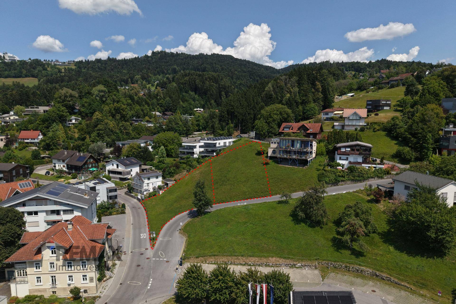 Übersicht aus der Luft des Baugrundstücks, umgeben von Häusern und grünen Hügeln im Hintergrund.