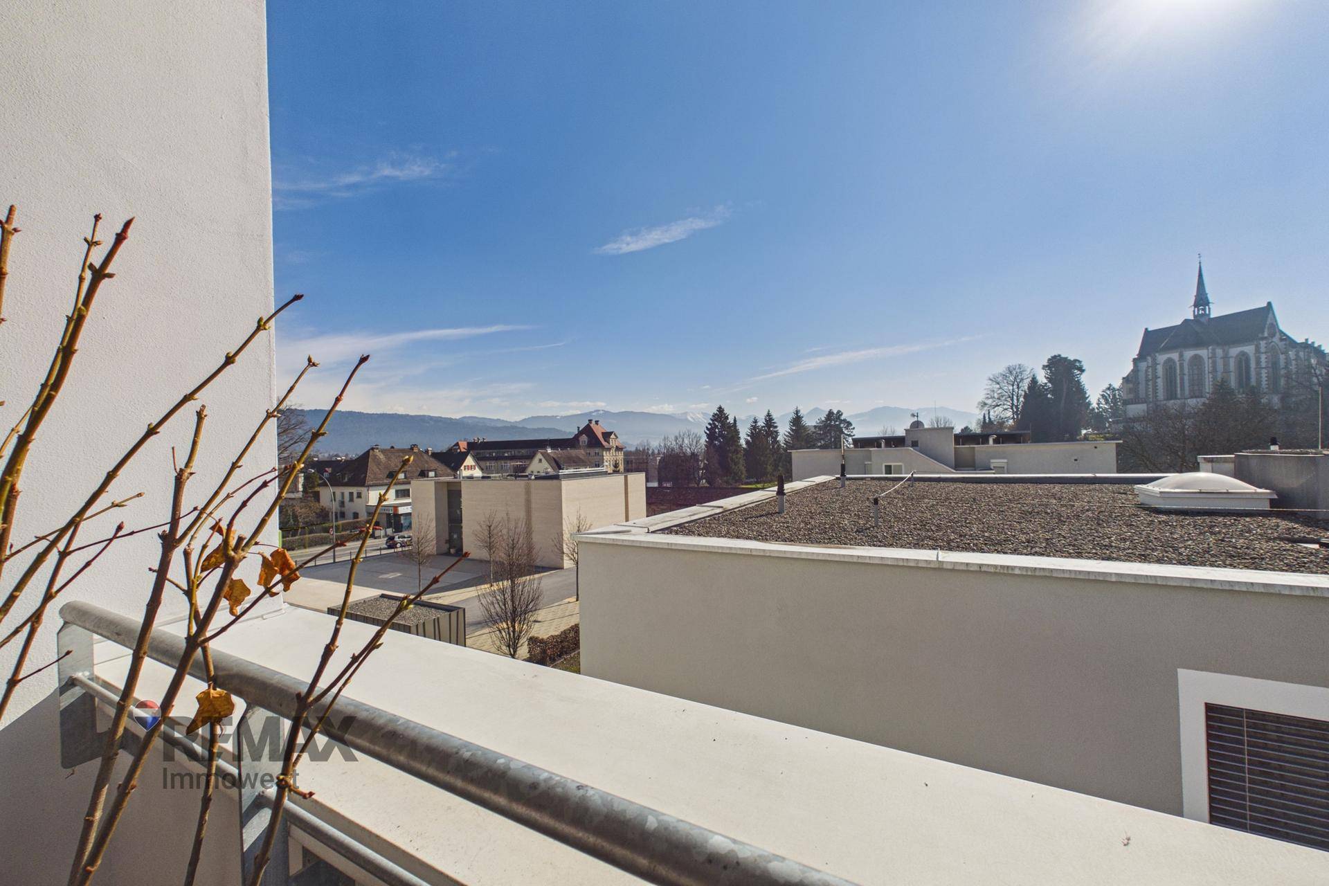 Panoramablick von einem Balkon über die Stadt, eine Kirche und die fernen Berge an einem klaren Tag.