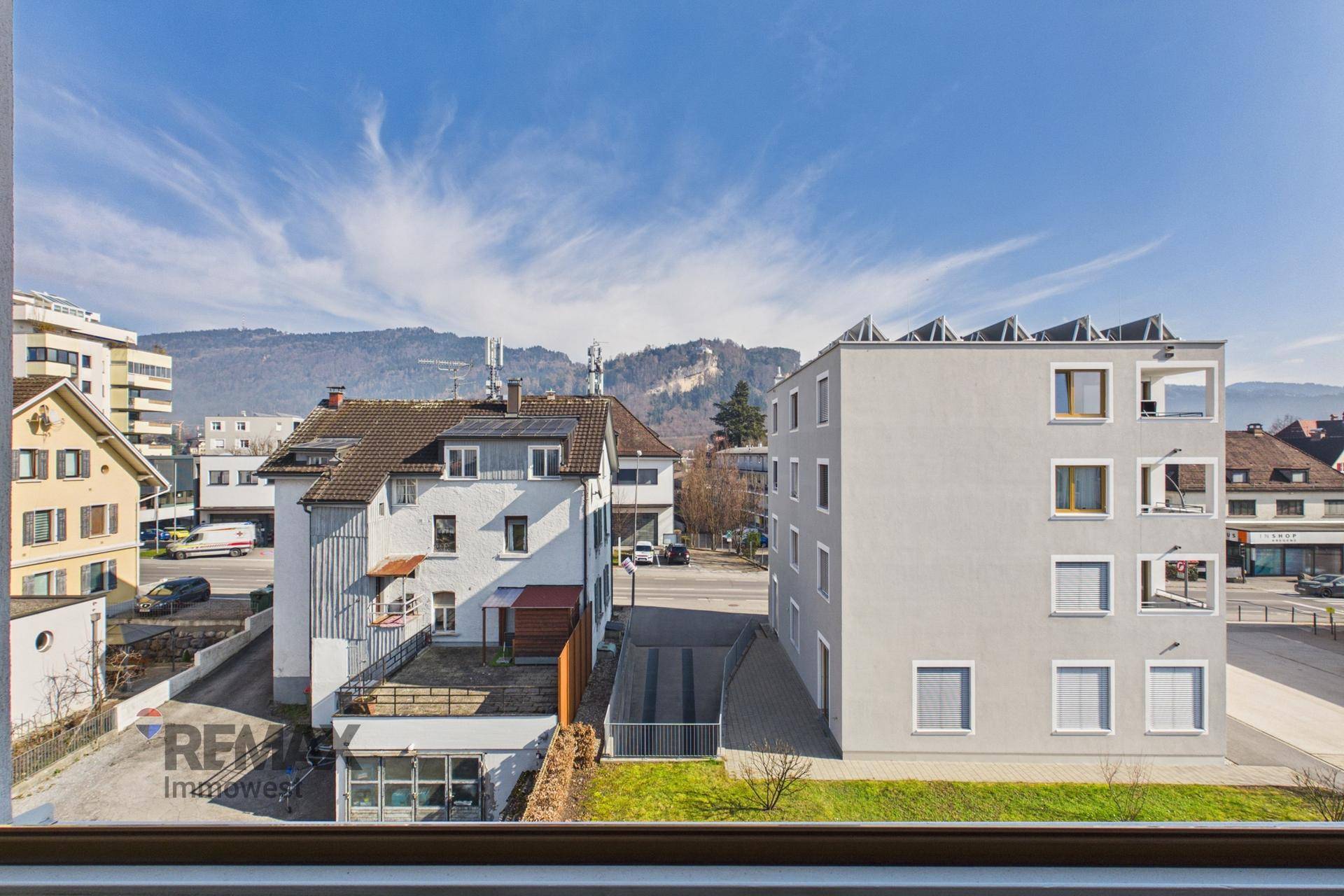 Blick aus dem Fenster auf die Nachbarschaft mit Gebäuden, Straße und fernen Bergen.
