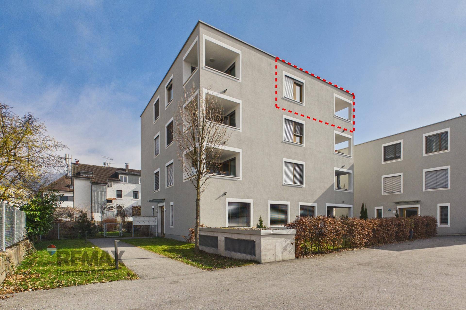 Modernes Mehrfamilienhaus mit grauer Fassade, Balkonen und gepflegter Grünanlage an einem sonnigen Tag.