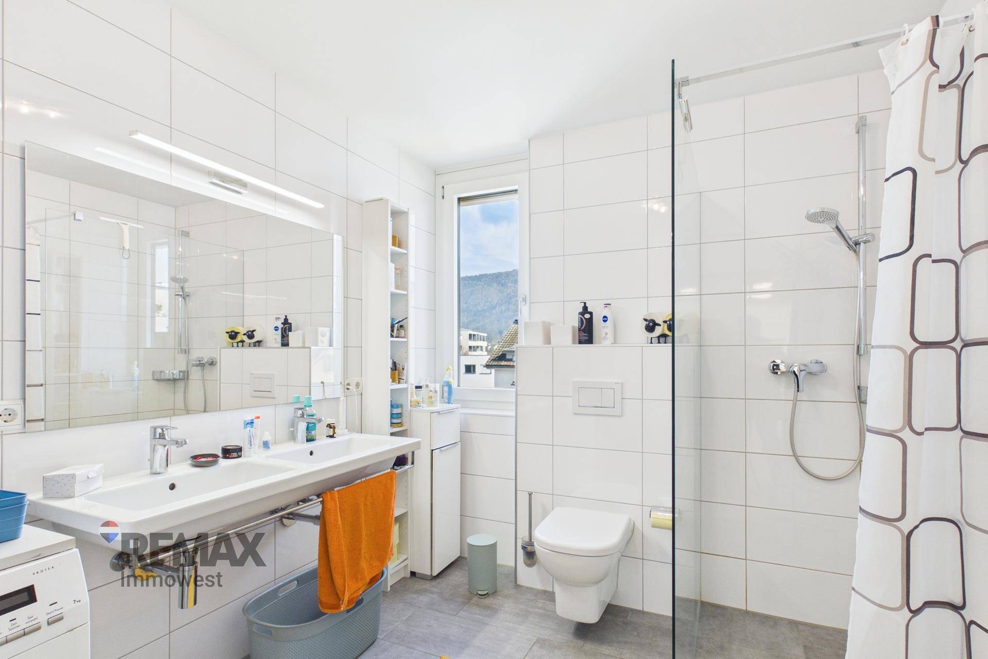 Modernes Badezimmer mit weißen Fliesen, Waschbecken, Toilette und einer begehbaren Dusche.