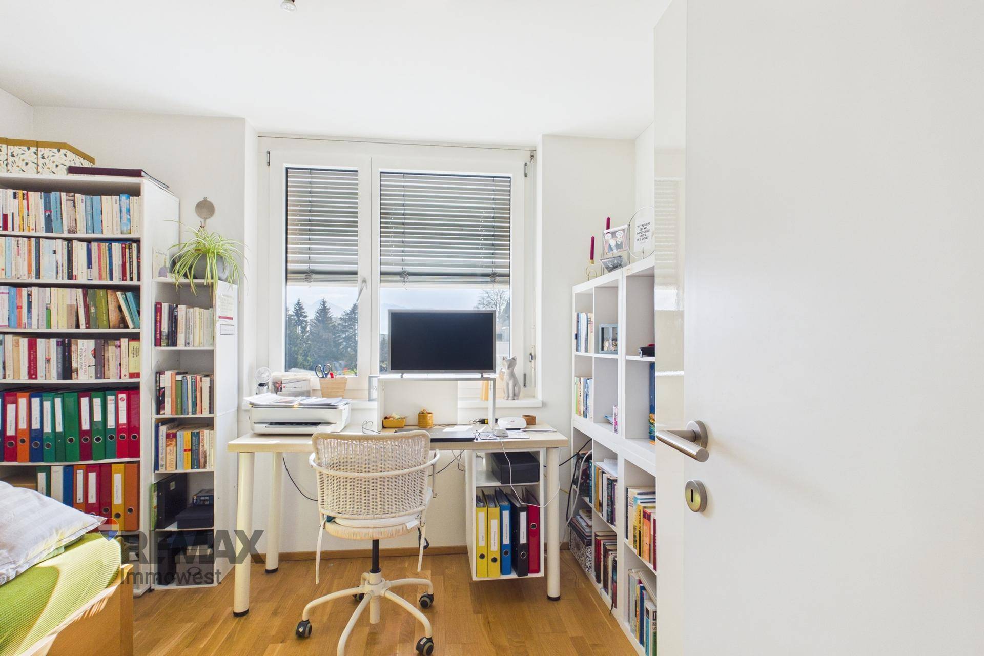 Funktionales Arbeitszimmer mit Schreibtisch, Bürostuhl und umfangreichen Bücherregalen am Fenster.