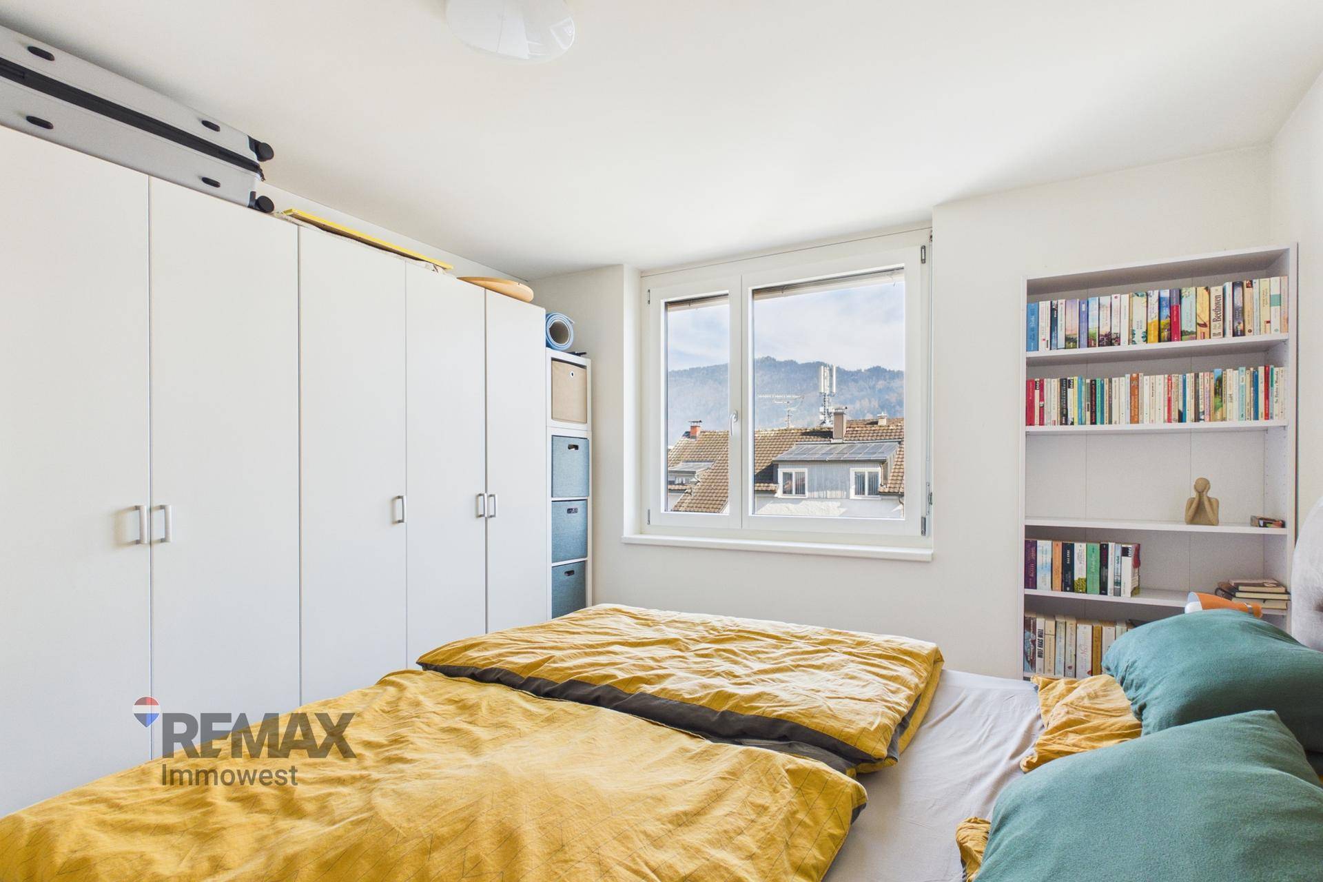 Schlafzimmer mit großem Bett, weißen Kleiderschränken und einem Fenster mit Blick auf die Umgebung.