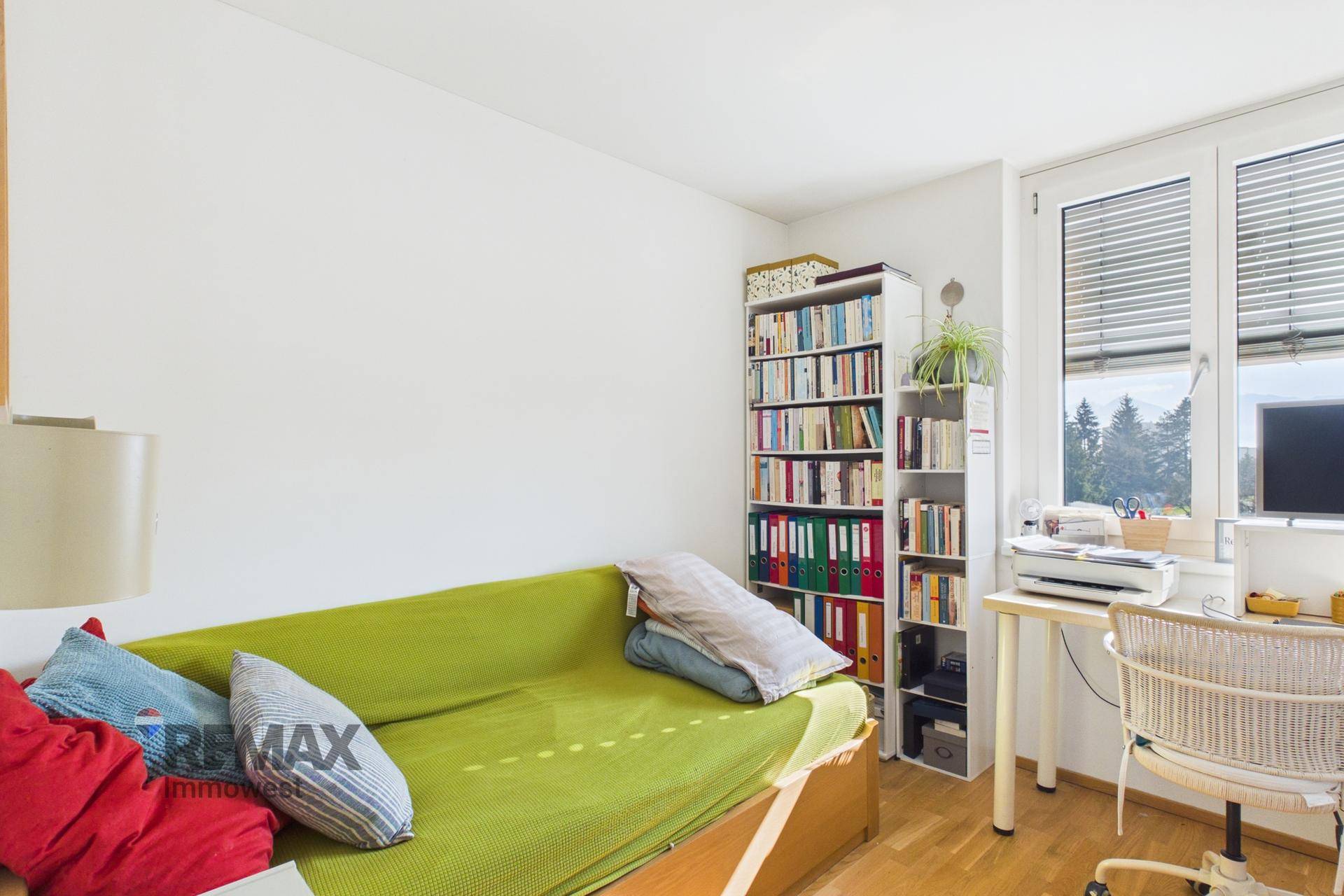 Helles Arbeitszimmer mit grünem Schlafsofa, Schreibtisch und Bücherregalen, ideal für Gäste.