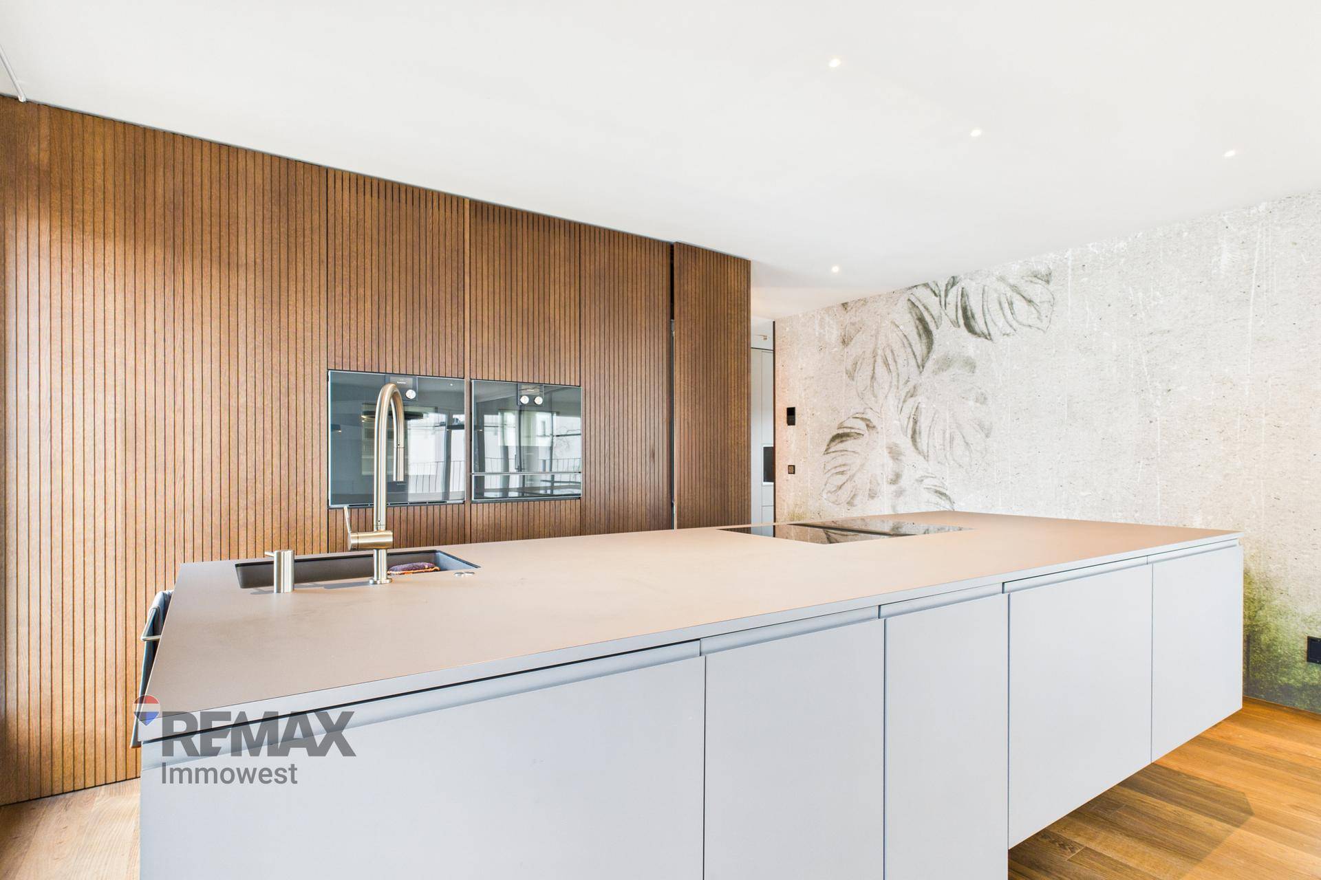 Elegante Küche mit Kücheninsel, integrierten Backöfen und einer dekorativen Wand mit Pflanzenmotiv.