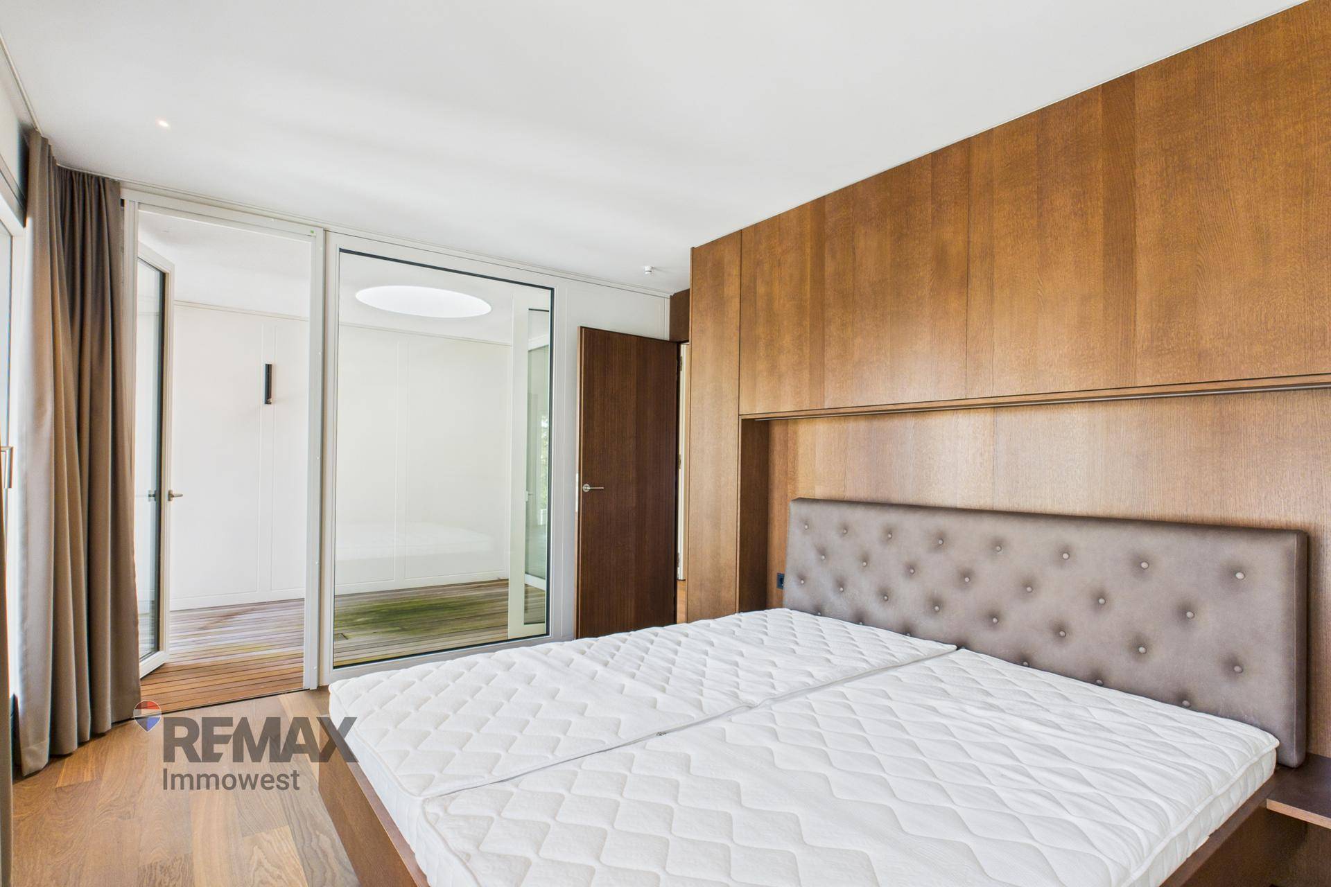 Schlafzimmer mit Holzboden, Holzwandverkleidung und Zugang zu einem angrenzenden Raum.