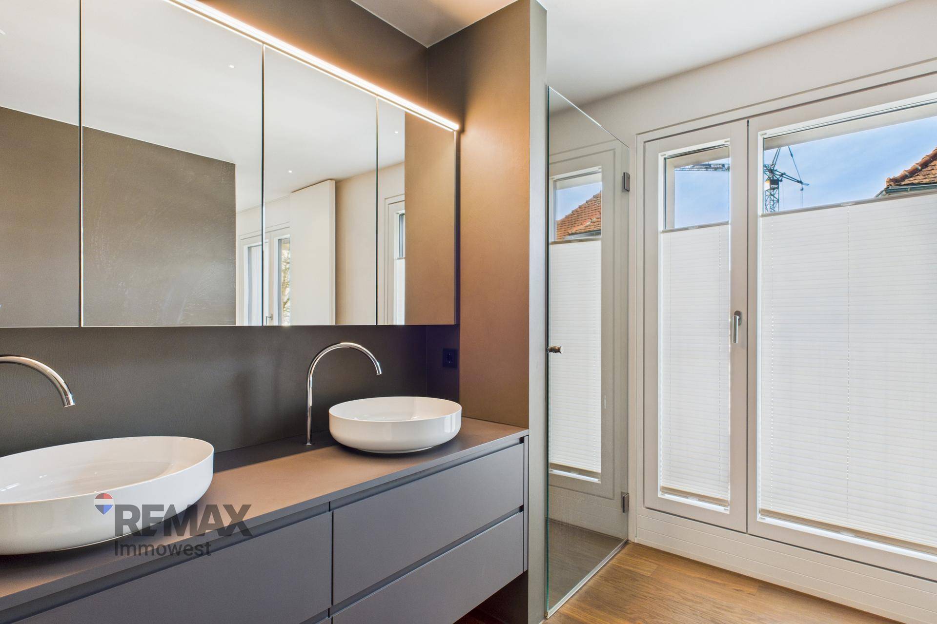 Modernes Badezimmer mit Doppelwaschbecken, Spiegelschrank und Fenster für Tageslicht.