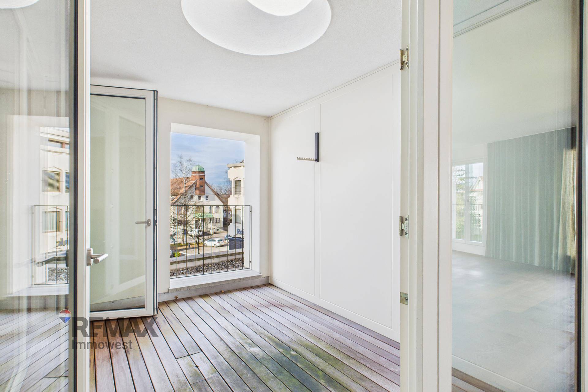 Heller Balkon mit Holzboden und Blick auf die umliegenden Gebäude und die Stadt.