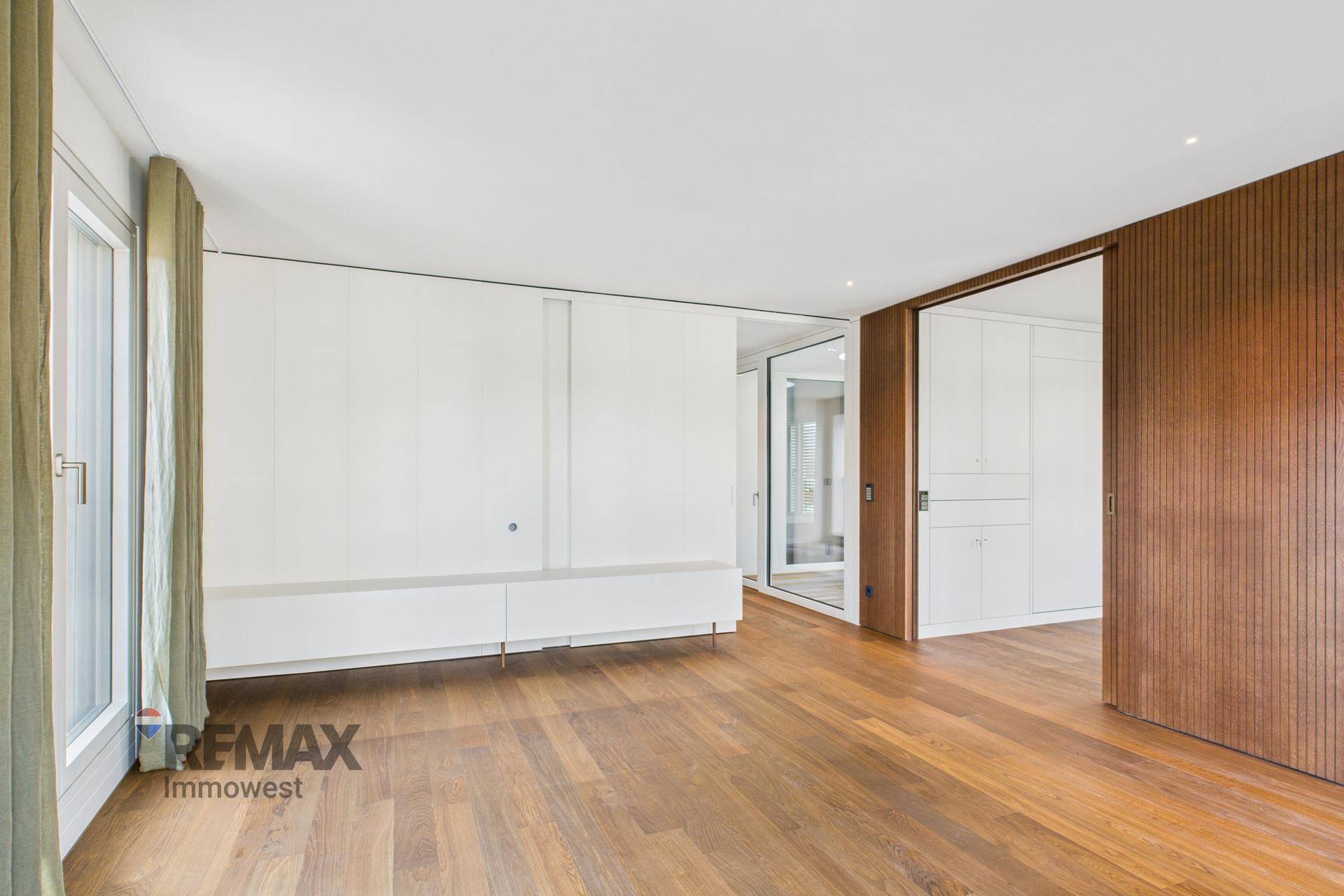 Helles Wohnzimmer mit Holzboden, Einbauschränken und einer Holzwandverkleidung.