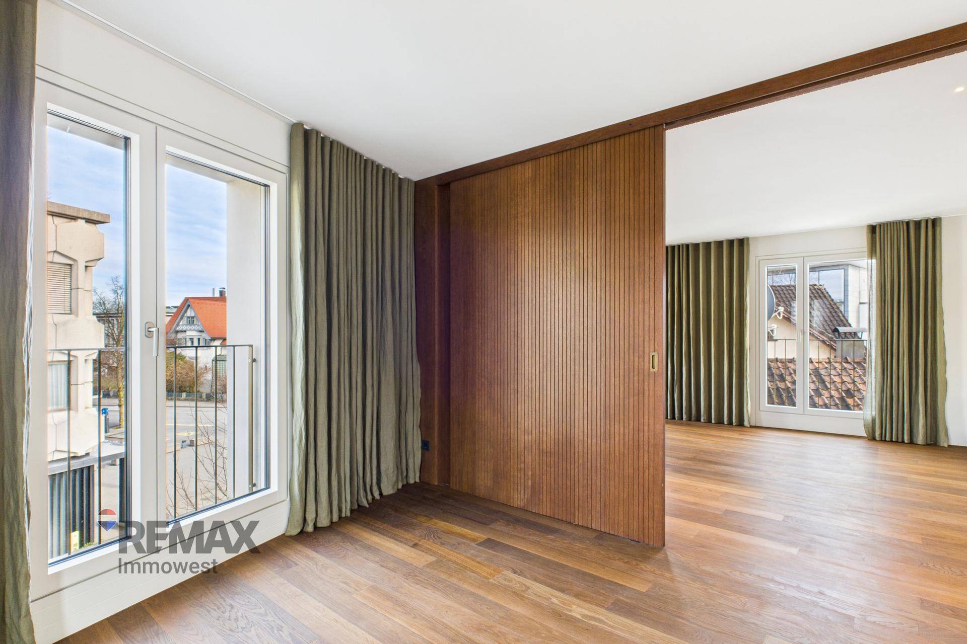 Wohnzimmer mit Holzboden, Schiebetür aus Holz und Zugang zu einem französischen Balkon.