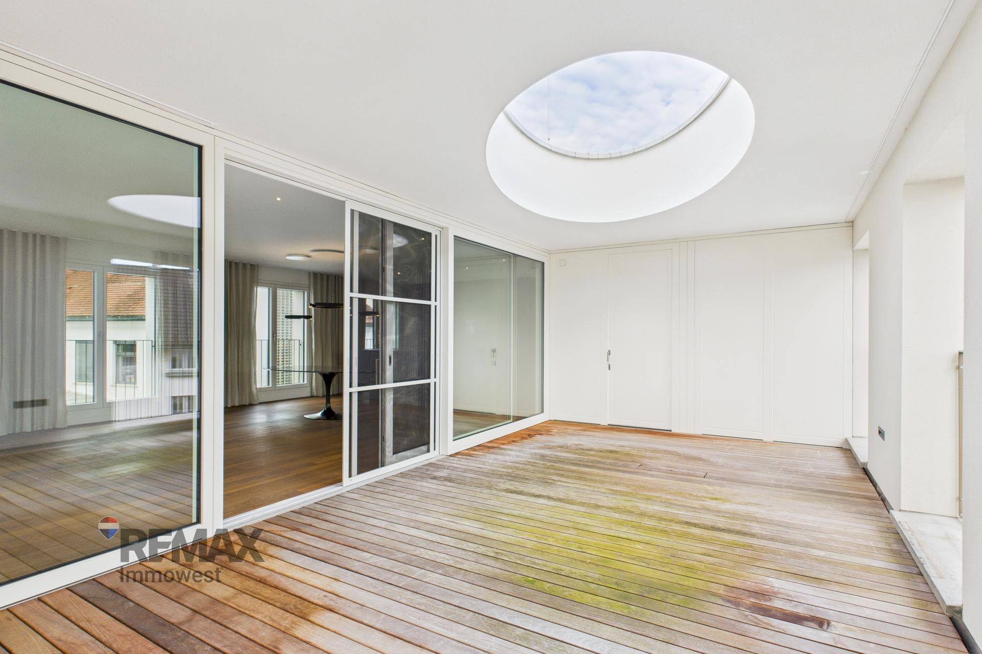 Große Terrasse mit Holzdeck, ovalem Oberlicht und Zugang zu den Innenräumen durch Glasschiebetüren.
