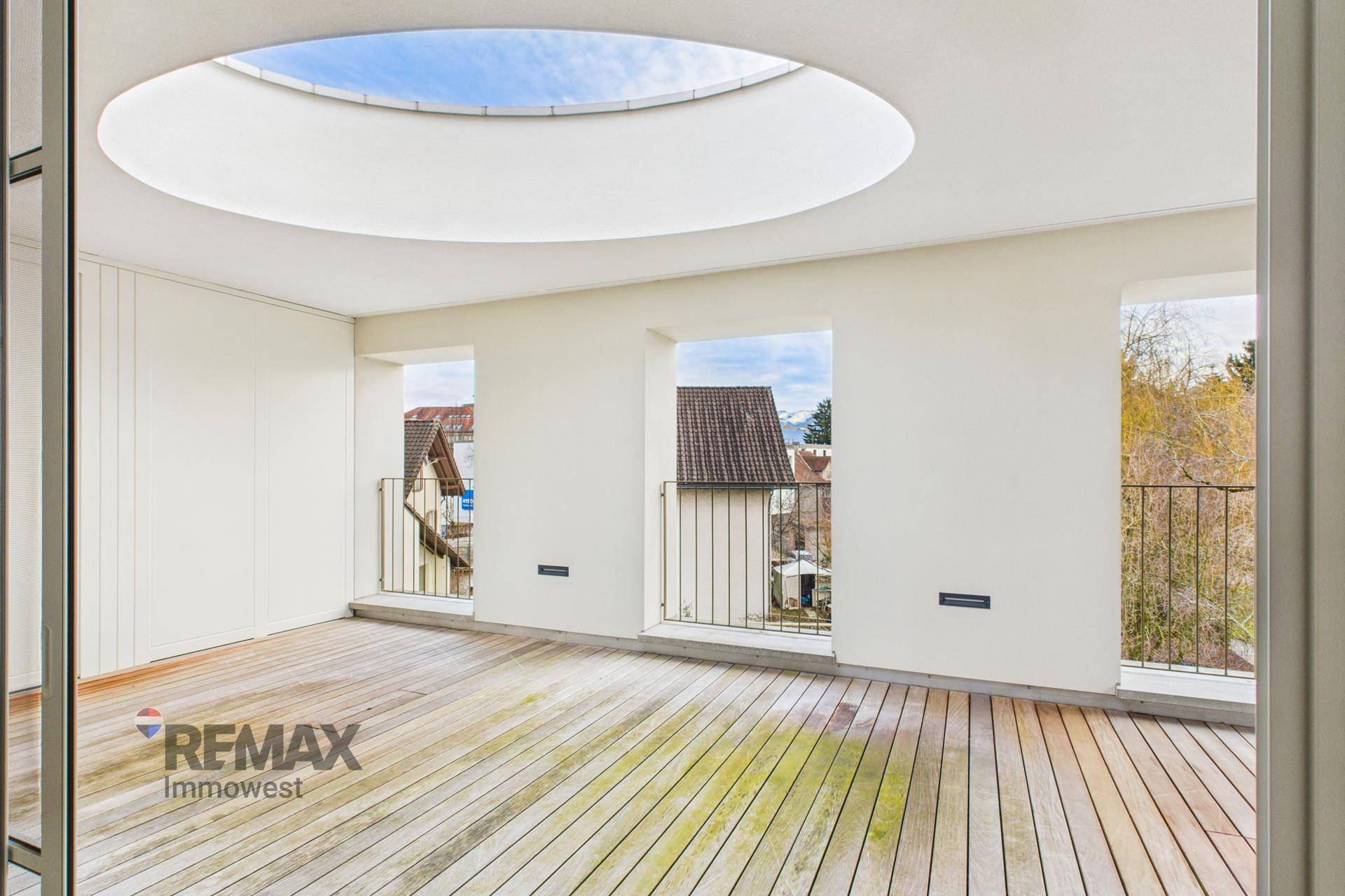 Geräumige Terrasse mit Holzdeck, ovalem Oberlicht und Blick auf die Umgebung durch kleine Fenster.