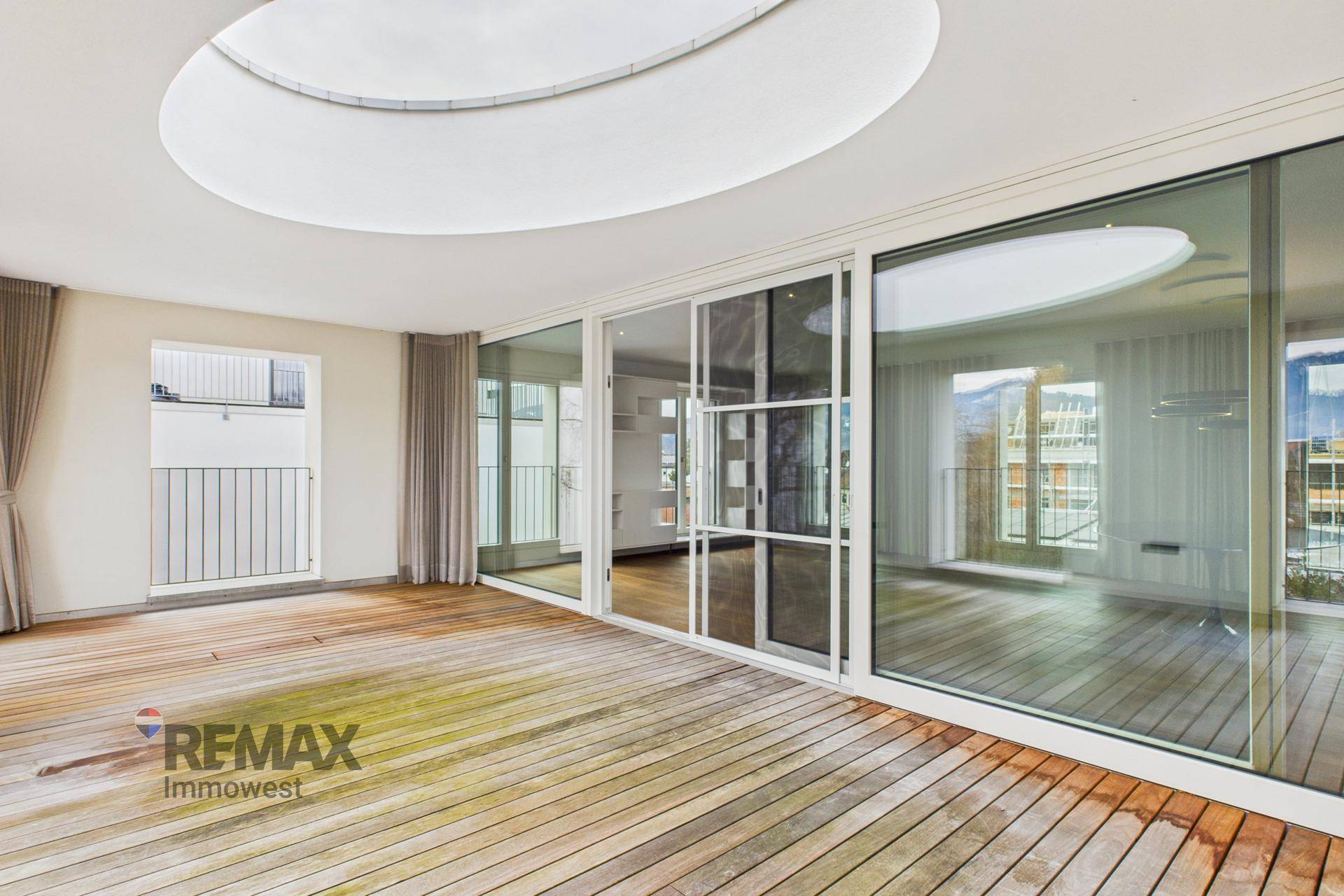 Weitläufige Terrasse mit Holzdeck, großzügigen Glasfronten und ovalem Oberlicht für viel Tageslicht.