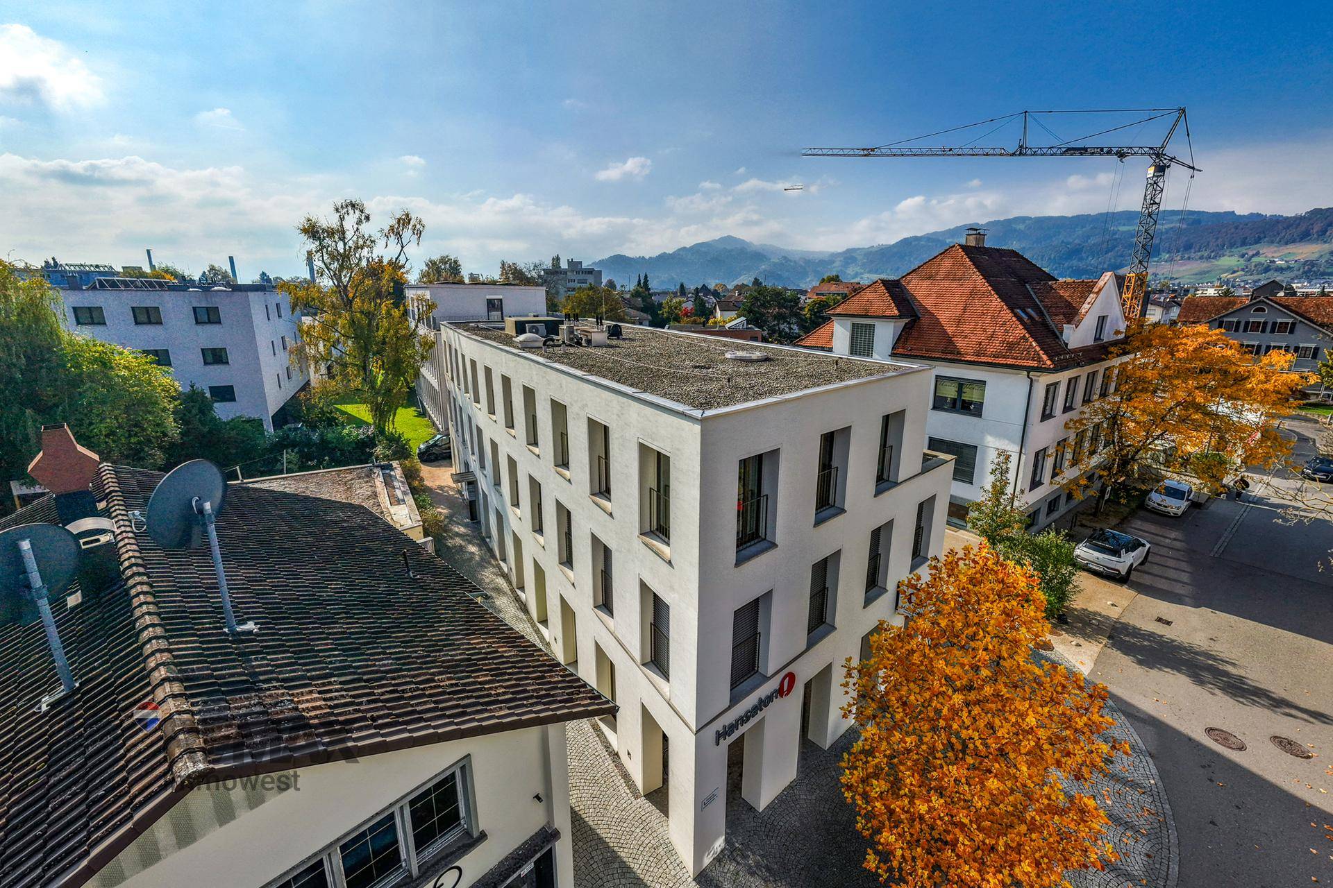 Luftaufnahme eines modernen Gebäudekomplexes mit umliegender Bebauung und Bergen im Hintergrund.