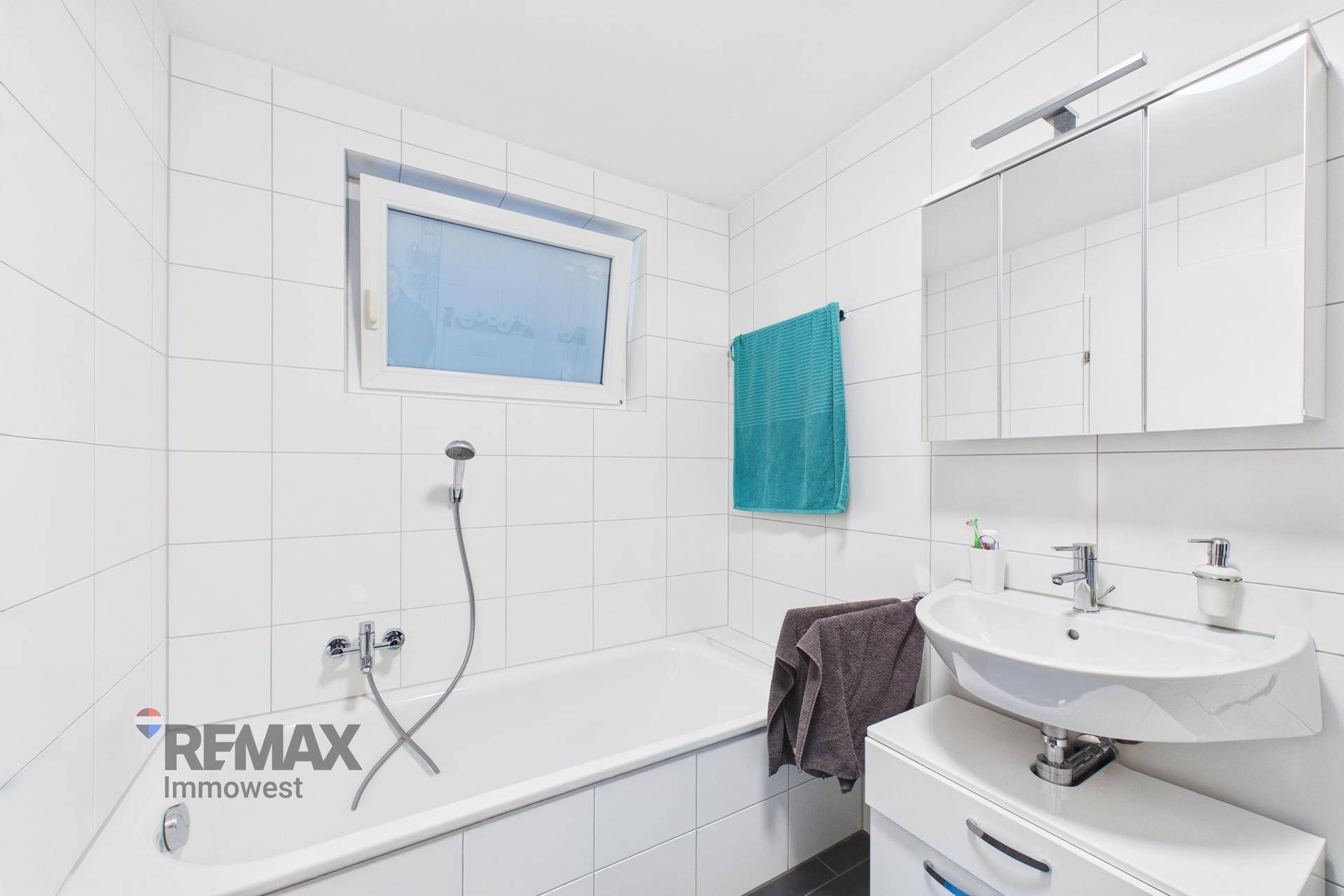 Helles Badezimmer mit Badewanne, Fenster und weißen Fliesen, funktional eingerichtet.