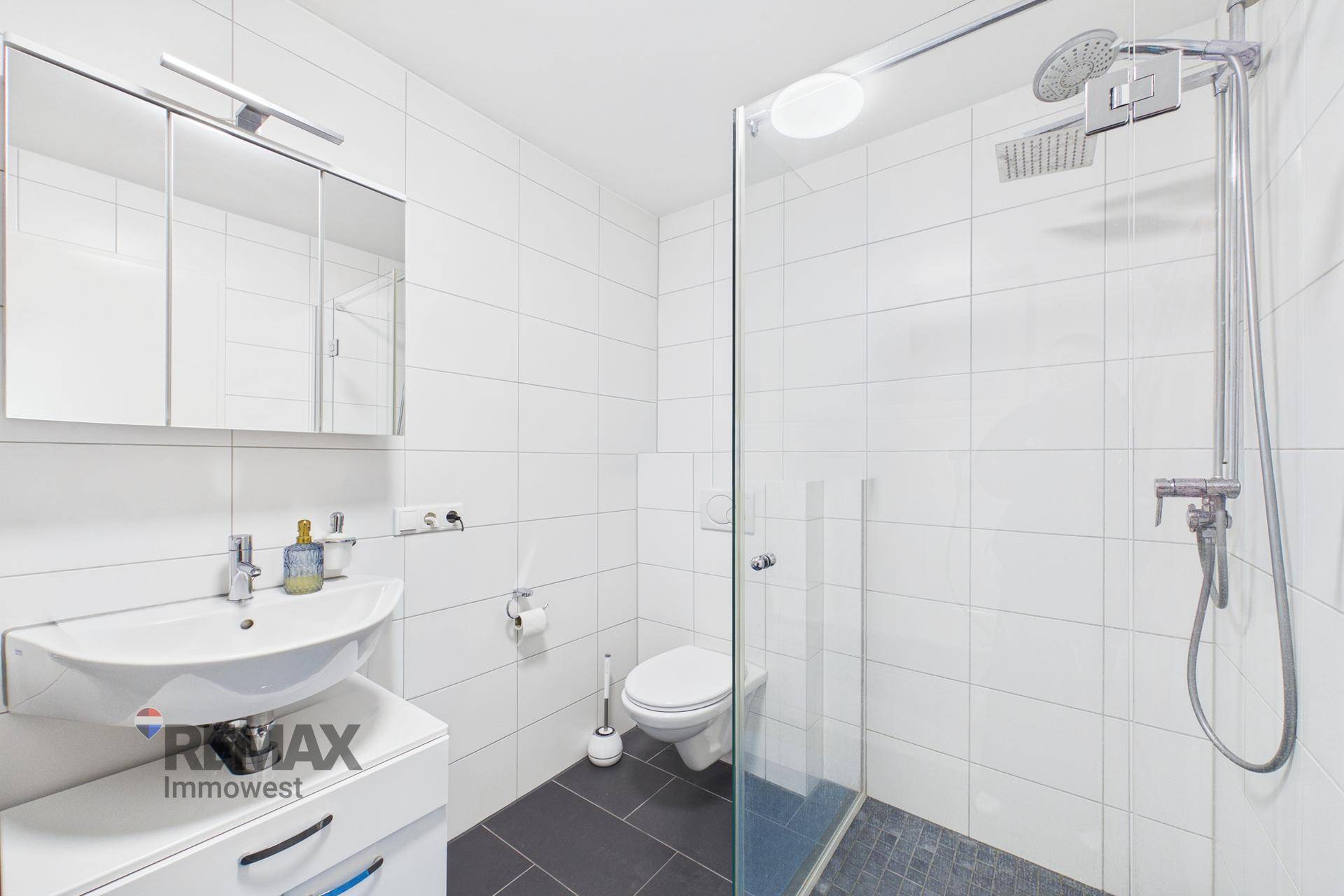 Modernes Badezimmer mit Duschkabine, WC und weißen Wandfliesen, praktisch gestaltet.