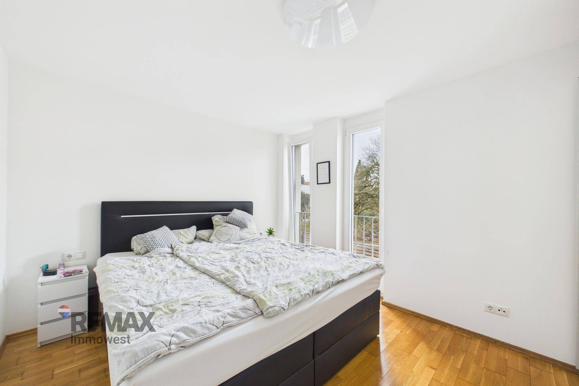 Schlafzimmer mit Doppelbett, Holzboden und Zugang zu einem französischen Balkon.