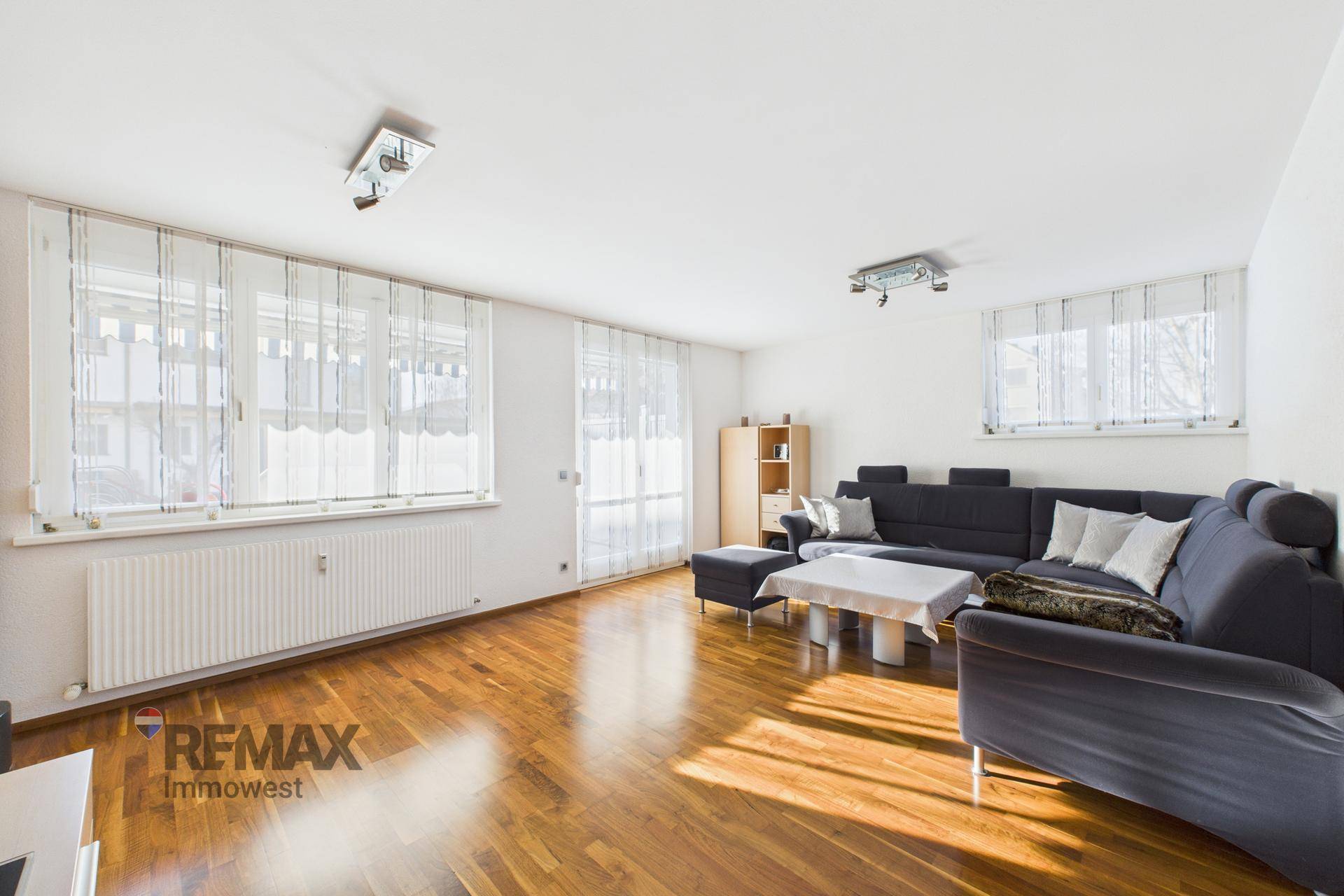 Helles Wohnzimmer mit großen Fenstern, Holzparkett und bequemer Sitzecke.