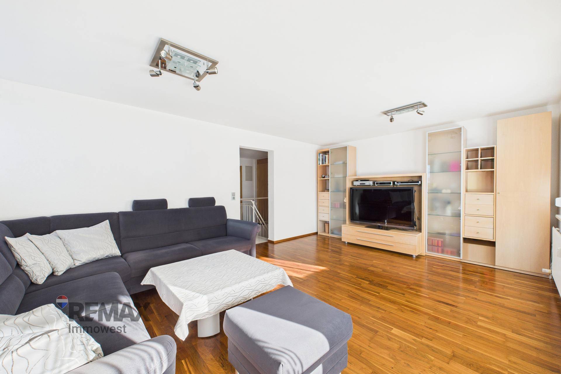 Geräumiges Wohnzimmer mit dunklem Sofa, Holzparkett und Medienmöbeln.