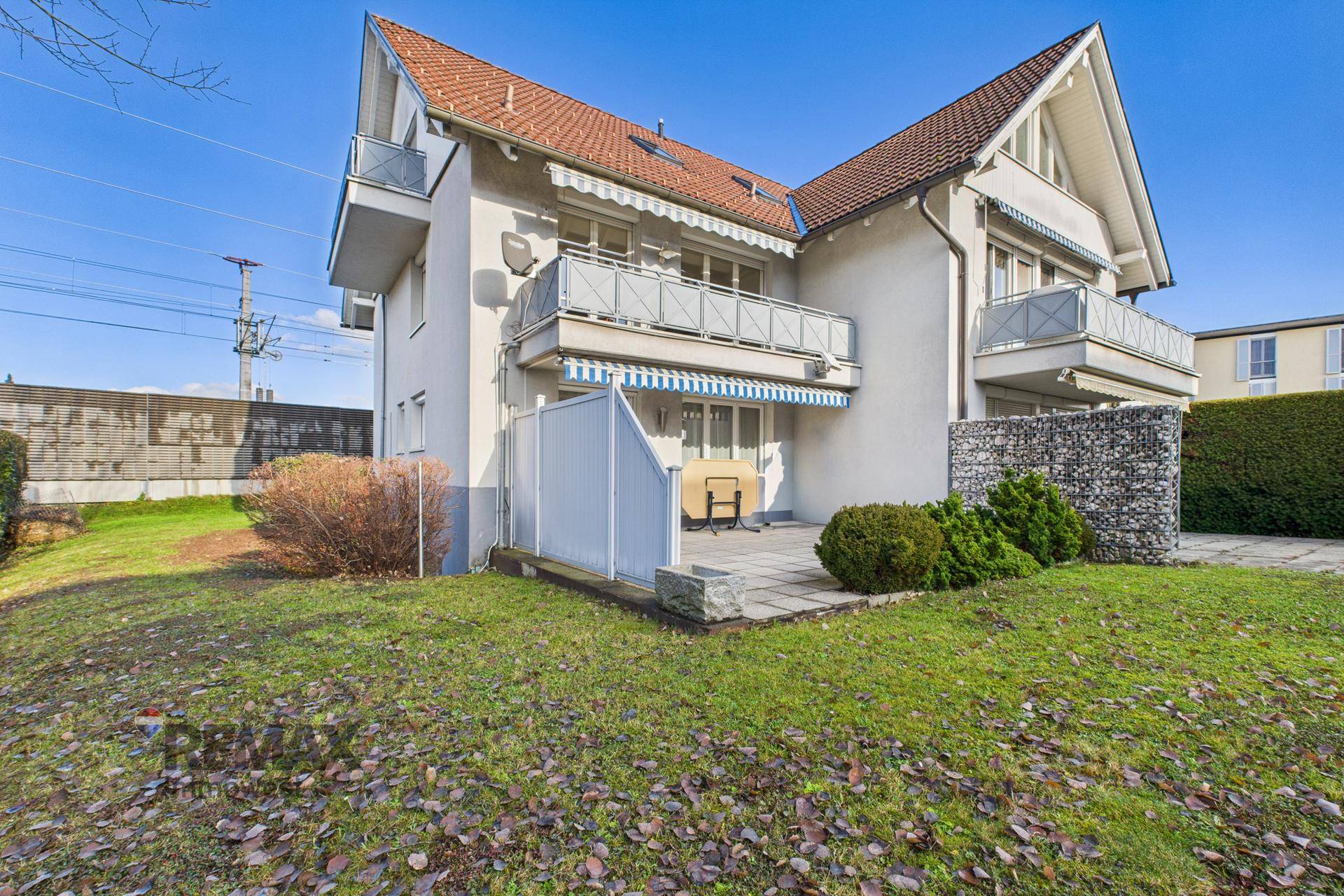 Außenansicht des Gebäudes mit gepflegtem Rasen, Terrasse und Balkonen unter blauem Himmel.