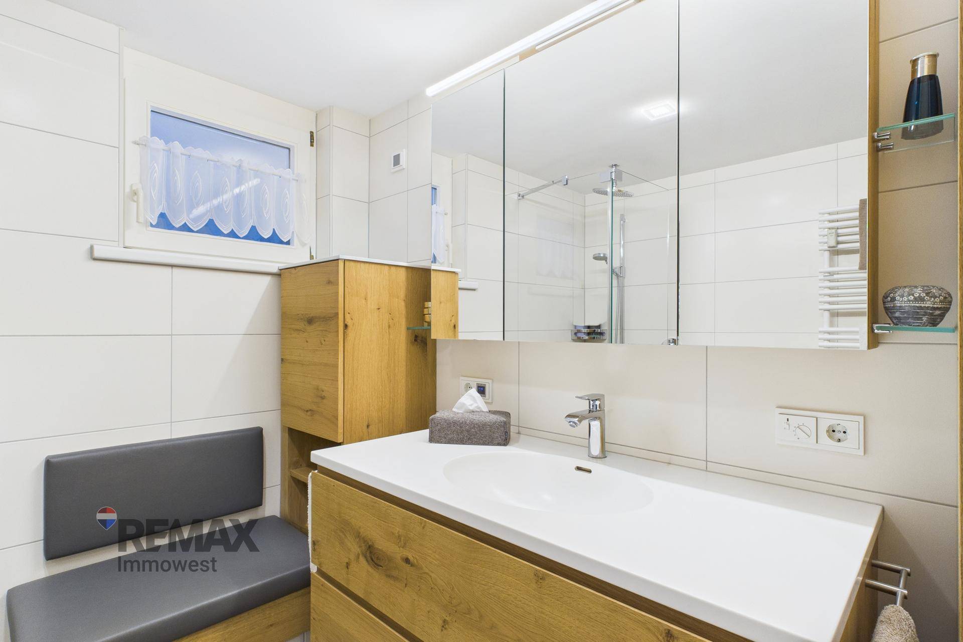 Helles Badezimmer mit Holzwaschtisch, Spiegelschrank, Dusche und Fenster.