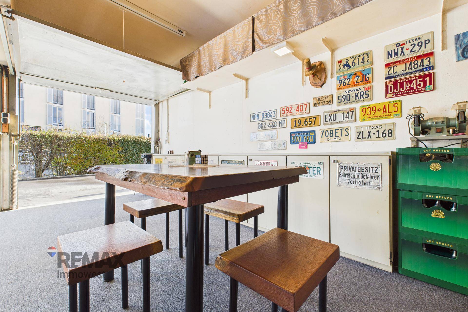 Garage mit Teppichboden, Tisch, Hockern und dekorativen Nummernschildern an der Wand.