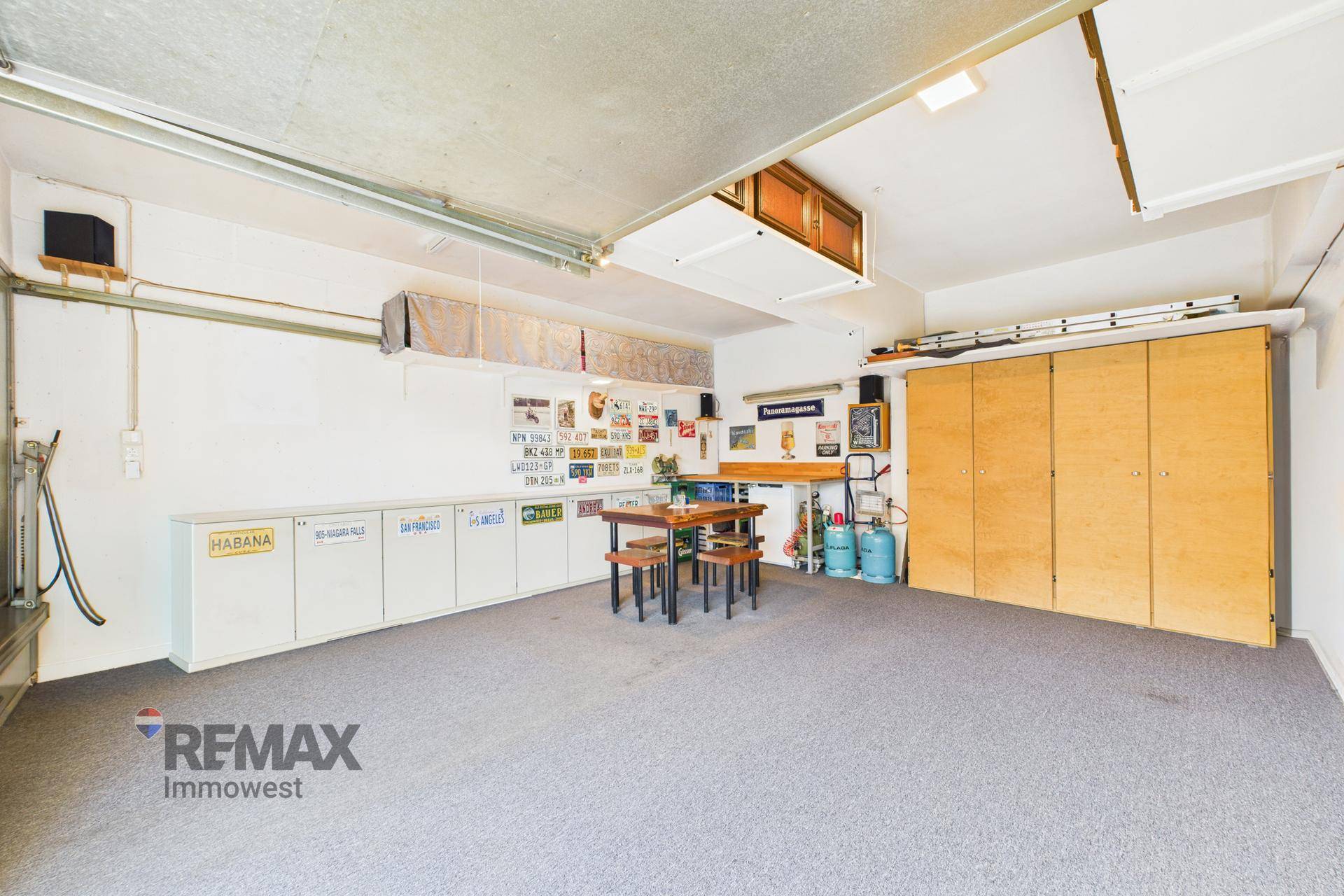 Geräumige Garage mit Teppichboden, viel Stauraum und einem Tisch mit Hockern.