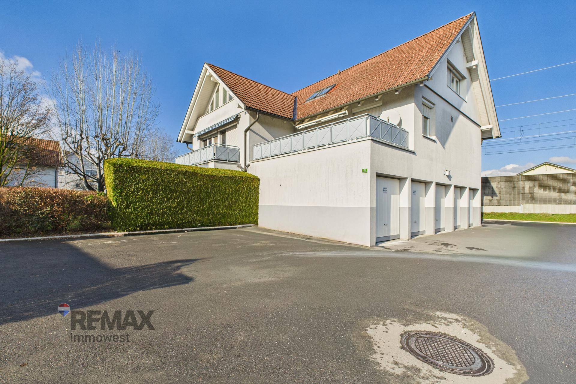 Rückansicht des Gebäudes mit Garagen, gepflegter Hecke und großem Parkplatz.