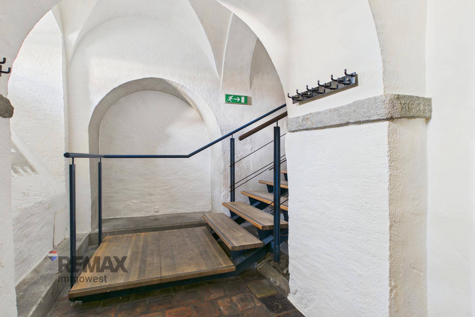 Unterer Bereich einer gewölbten Treppe mit Garderobenhaken und Ziegelboden.